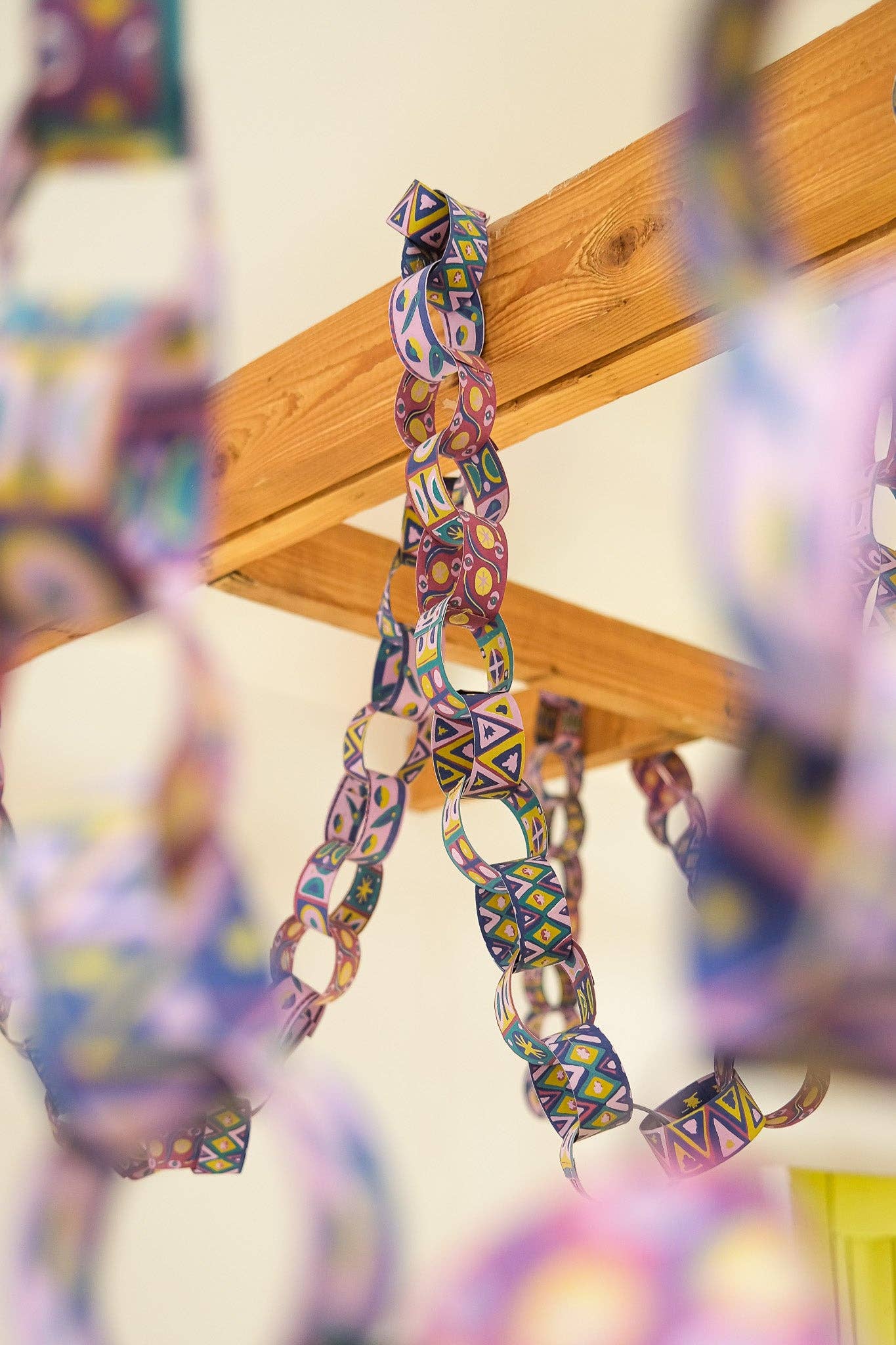 Colourful paper chain hanging from a wooden beam with a blurred background.