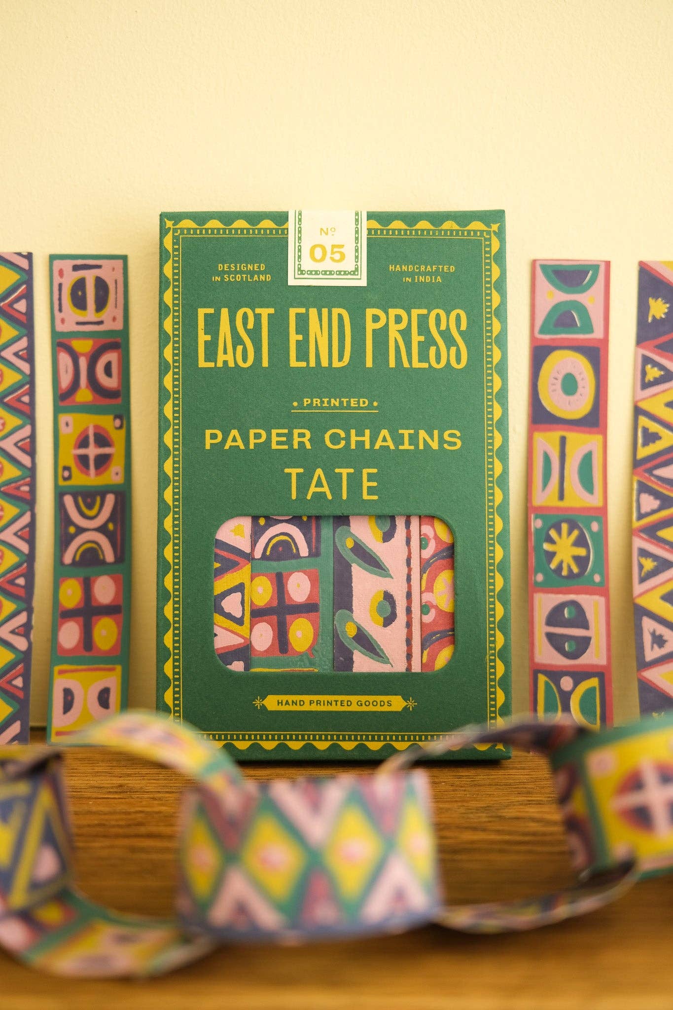 Packaging of East End Press paper chains with colourful geometric patterns on a wooden surface.