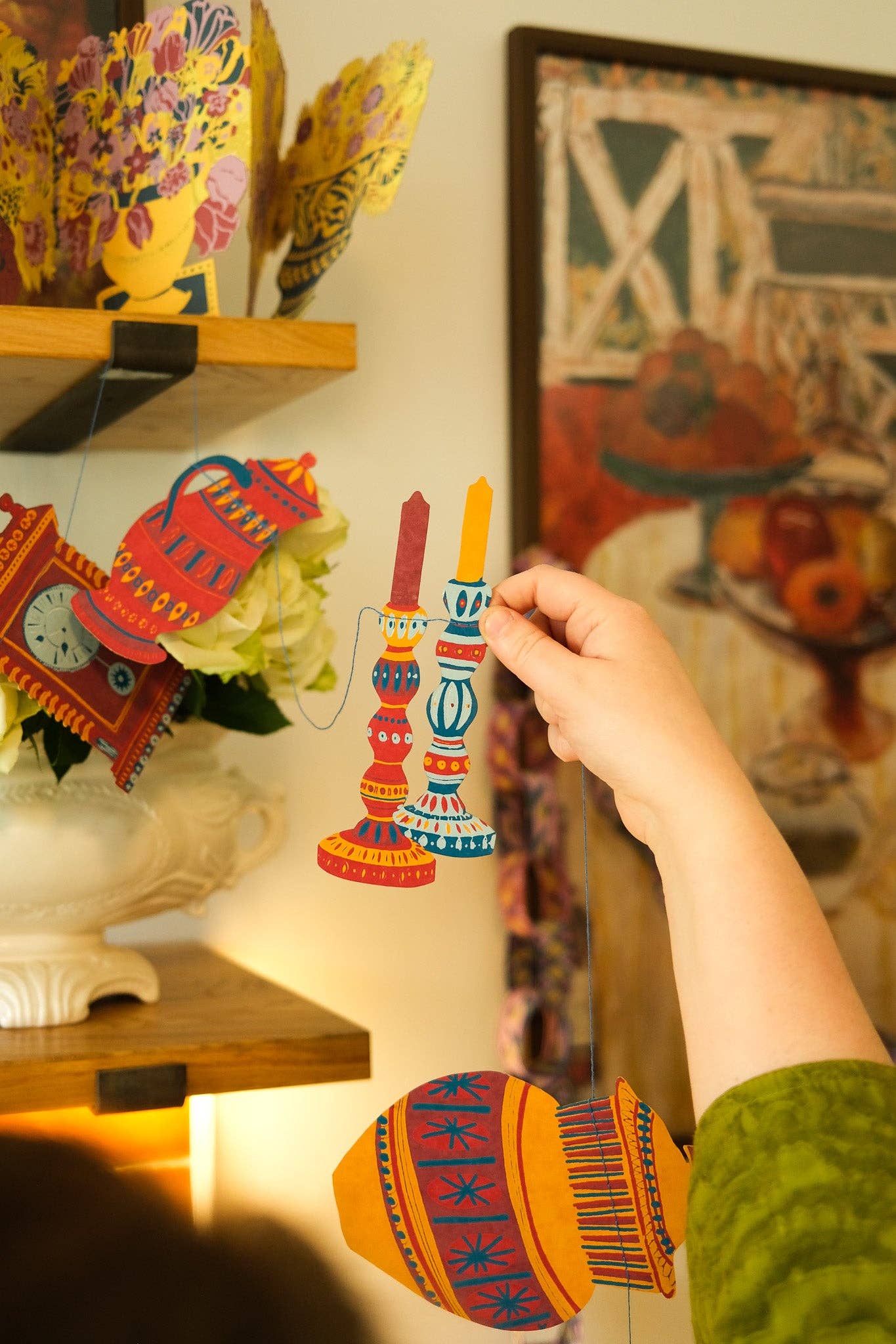 Hand holding a colourful candle garland in a decorated room in the background.