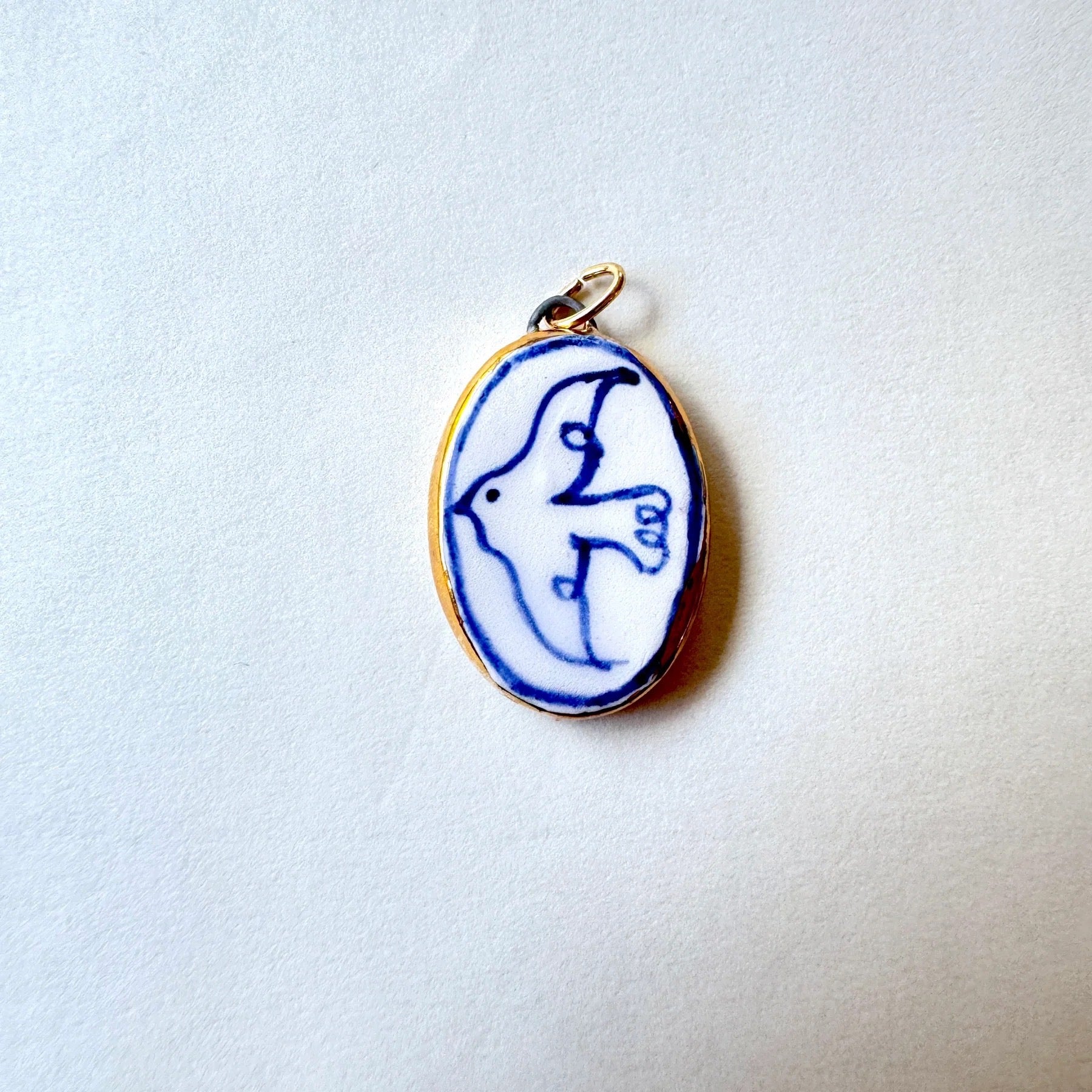 Oval pendant with blue and white dove on a light grey background.