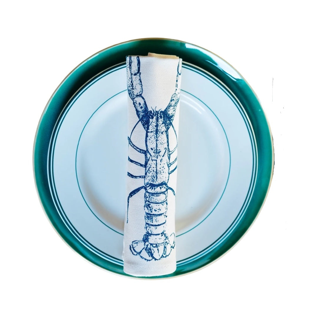 Cream cotton napkin with a blue lobster rolled and sitting on a plate.