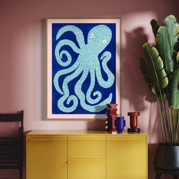 Framed octopus artwork on a pink wall with a yellow cabinet and decorative items.