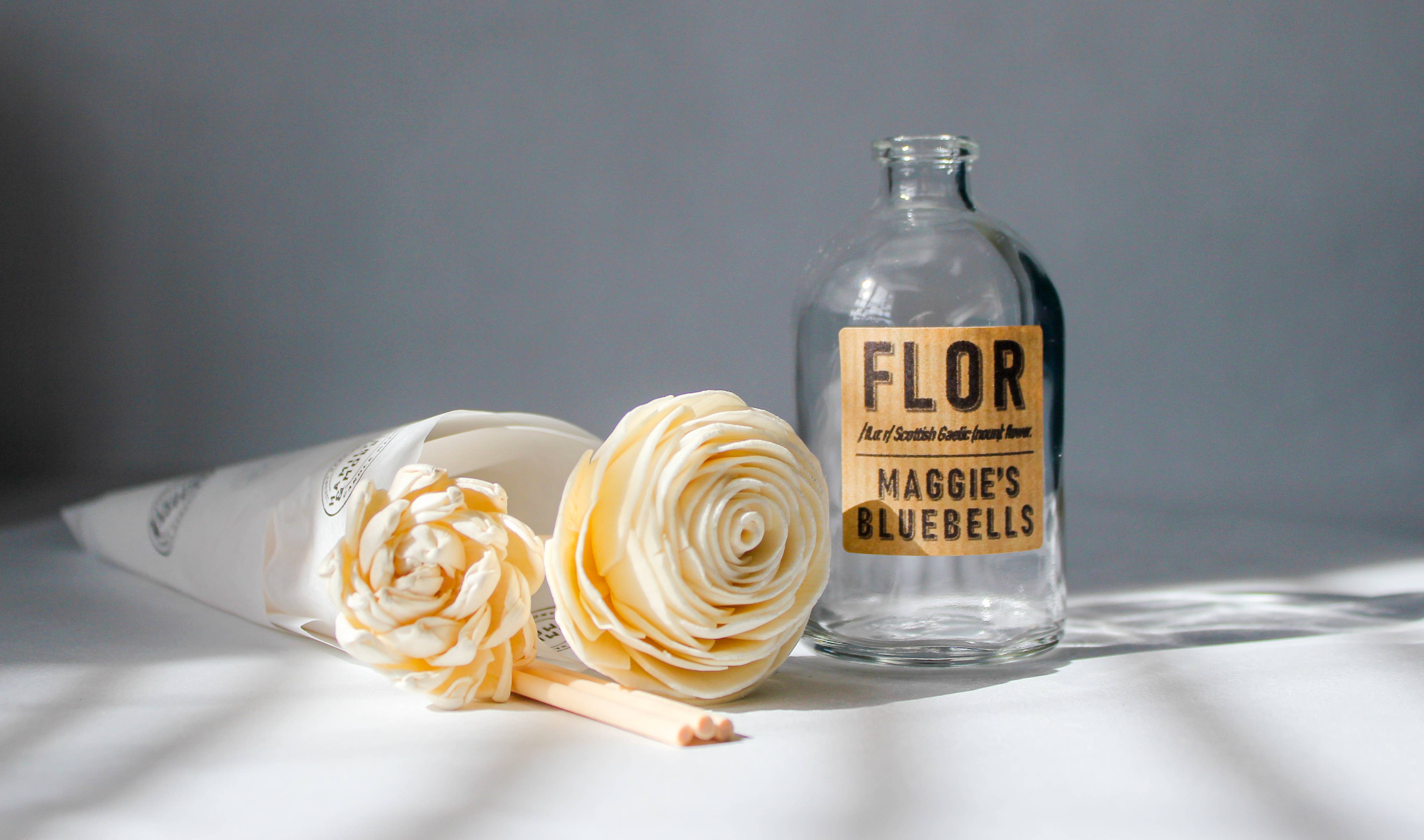 Glass bottle labeled 'FLOR' with decorative flowers on a gray background.