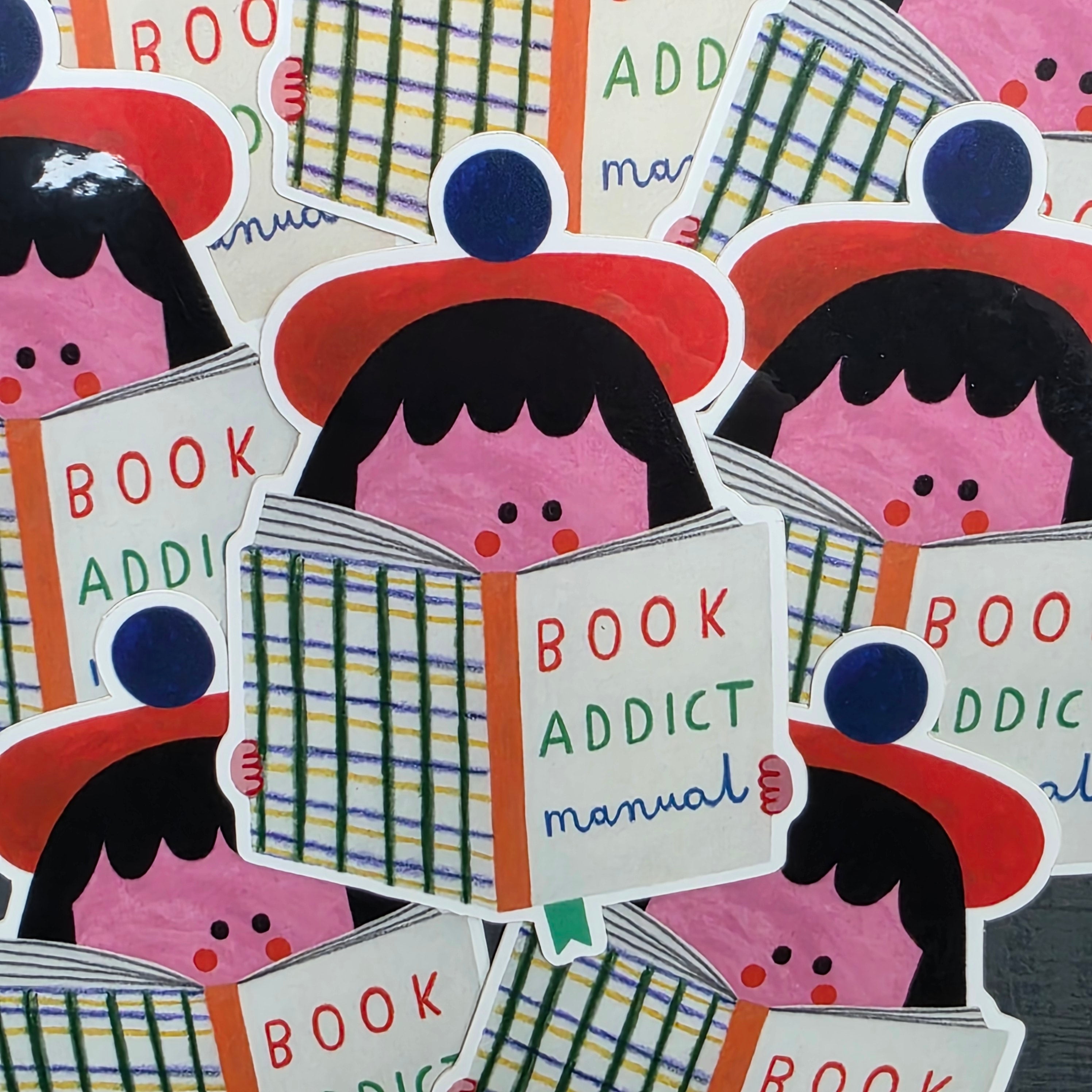 Vinyl sticker with a girl in a red beret with her face in a book called 'Book Addict Manual'.