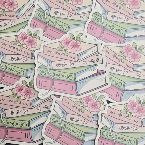 A sticker featuring an illustration of a stack of pastel coloured books with two pink flowers sitting on the top.
