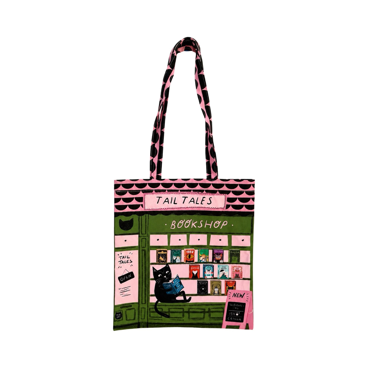 A tote bag featuring a colourful illustration of a bookshop storefront with the text 'TAIL TALES BOOKSHOP' and a black cat sitting outside. The bag has pink and black patterned shoulder straps and is shown on a plain white background.