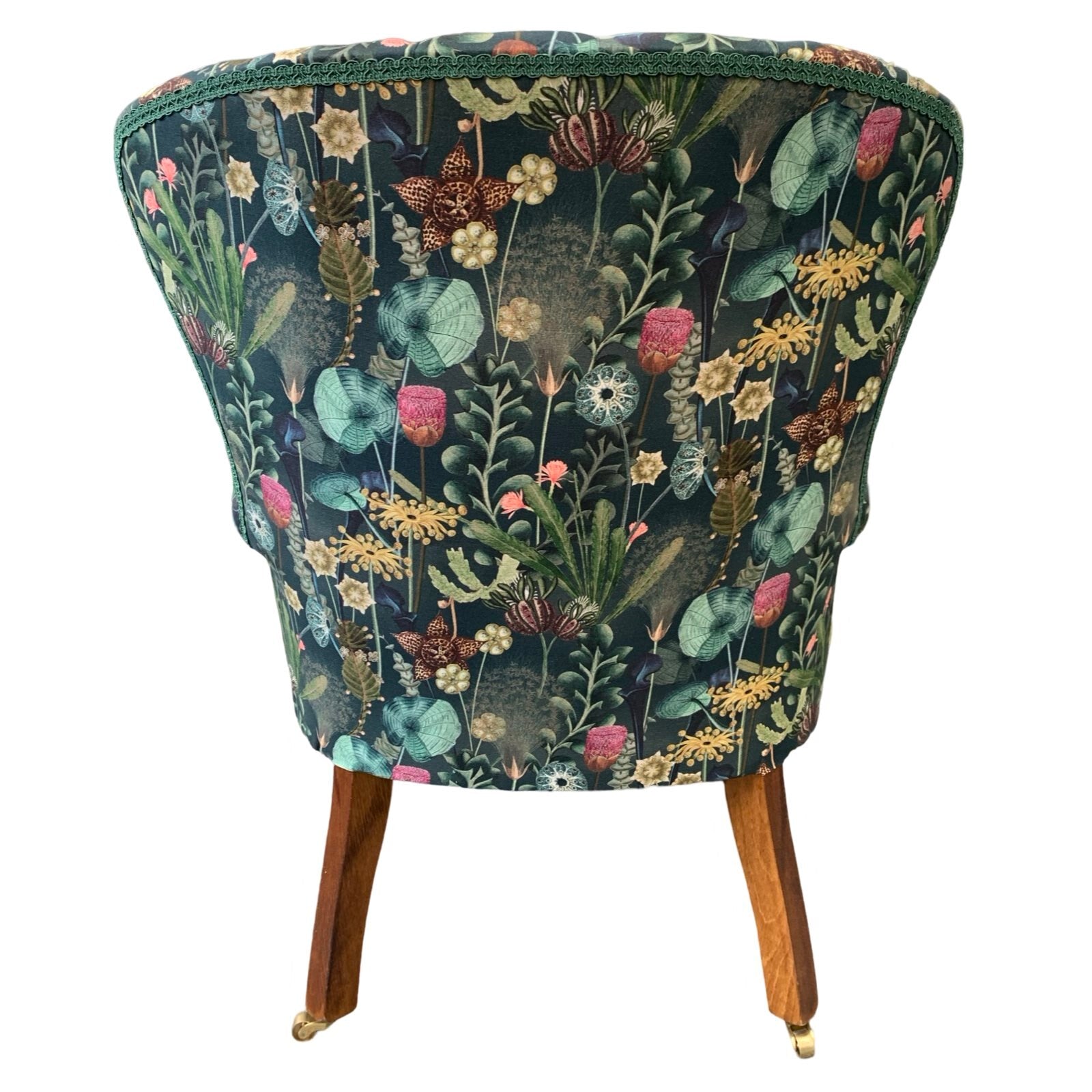 A dark green linen armchair with a turquoise, mustard, pink, and green botanical design, featuring a button-back and mahogany legs with gold castors.