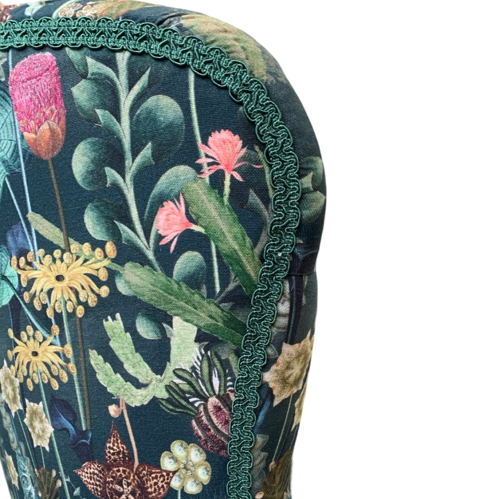 A dark green linen armchair with a turquoise, mustard, pink, and green botanical design, featuring a button-back and mahogany legs with gold castors.