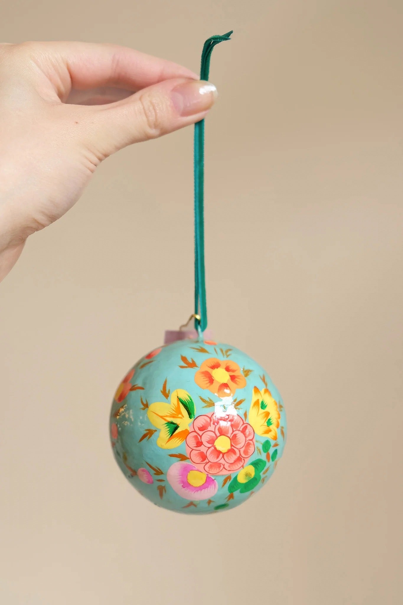 Decorative ornament with floral design held by a hand against a beige background.