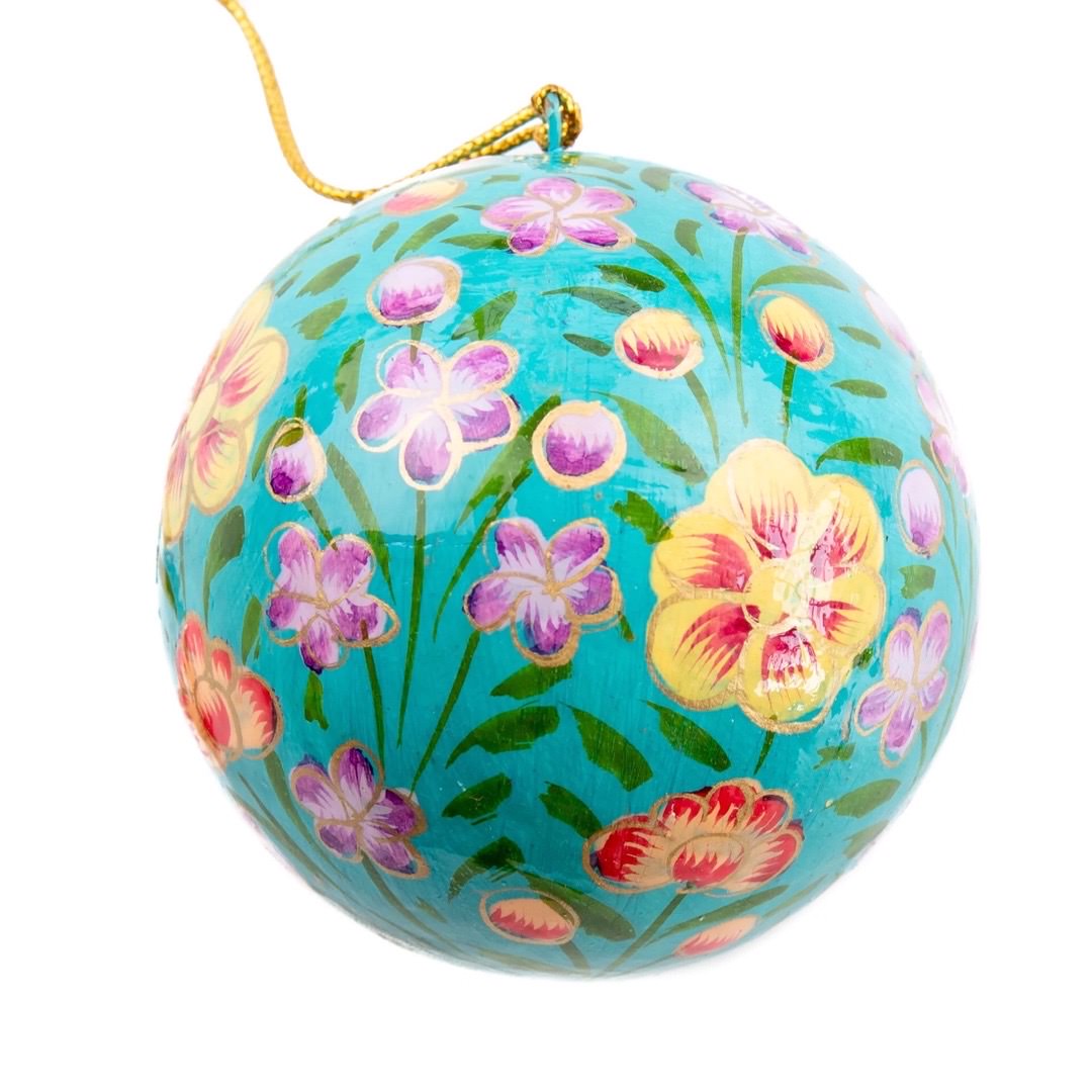 A round papier mache bauble in turquoise with a lilac, yellow and red floral design.