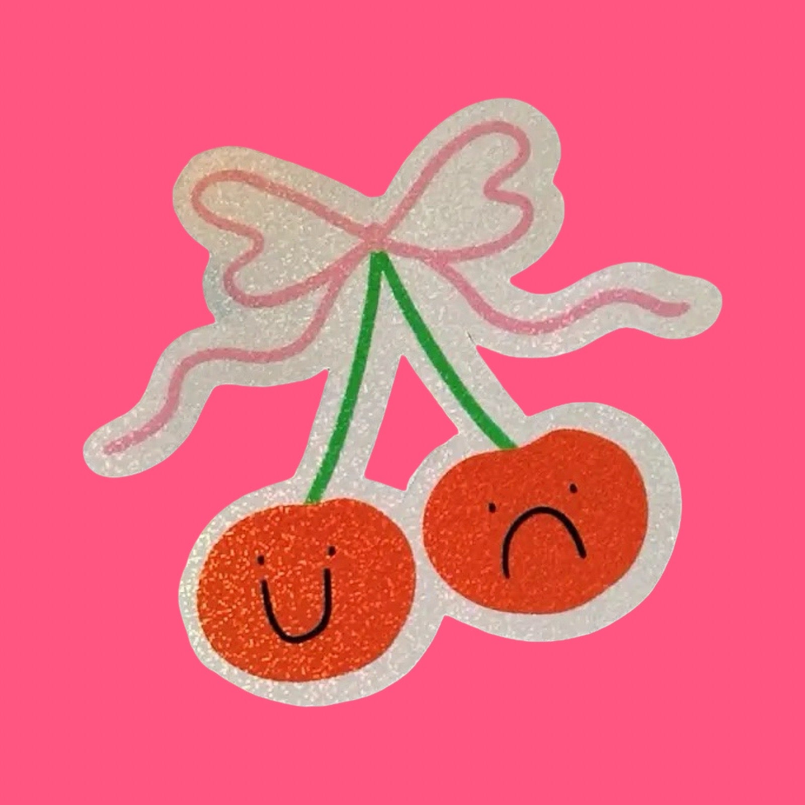 Two cherries with faces and a bow on a pink background.