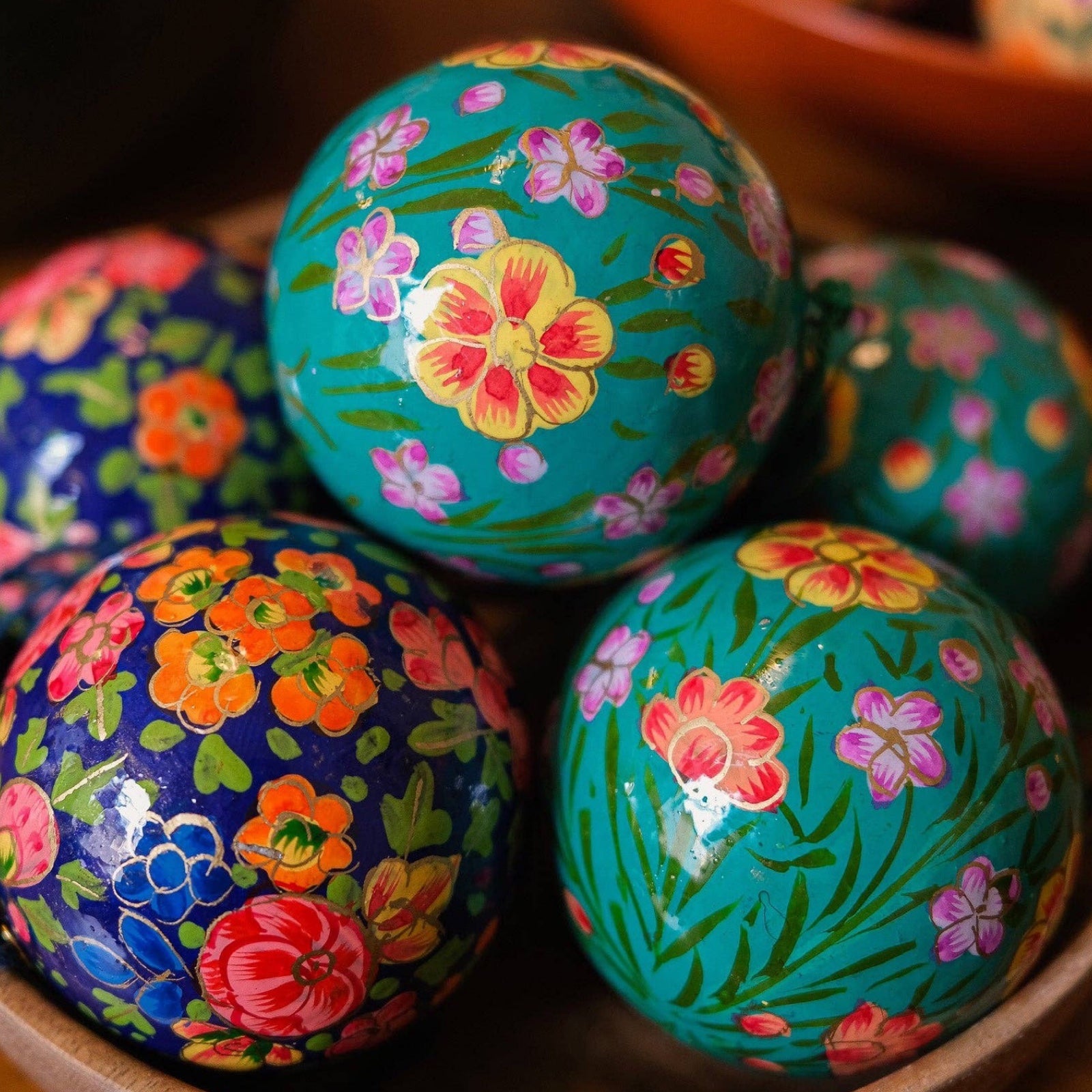A bowl of turquoise and navy floral papier mache baubles.