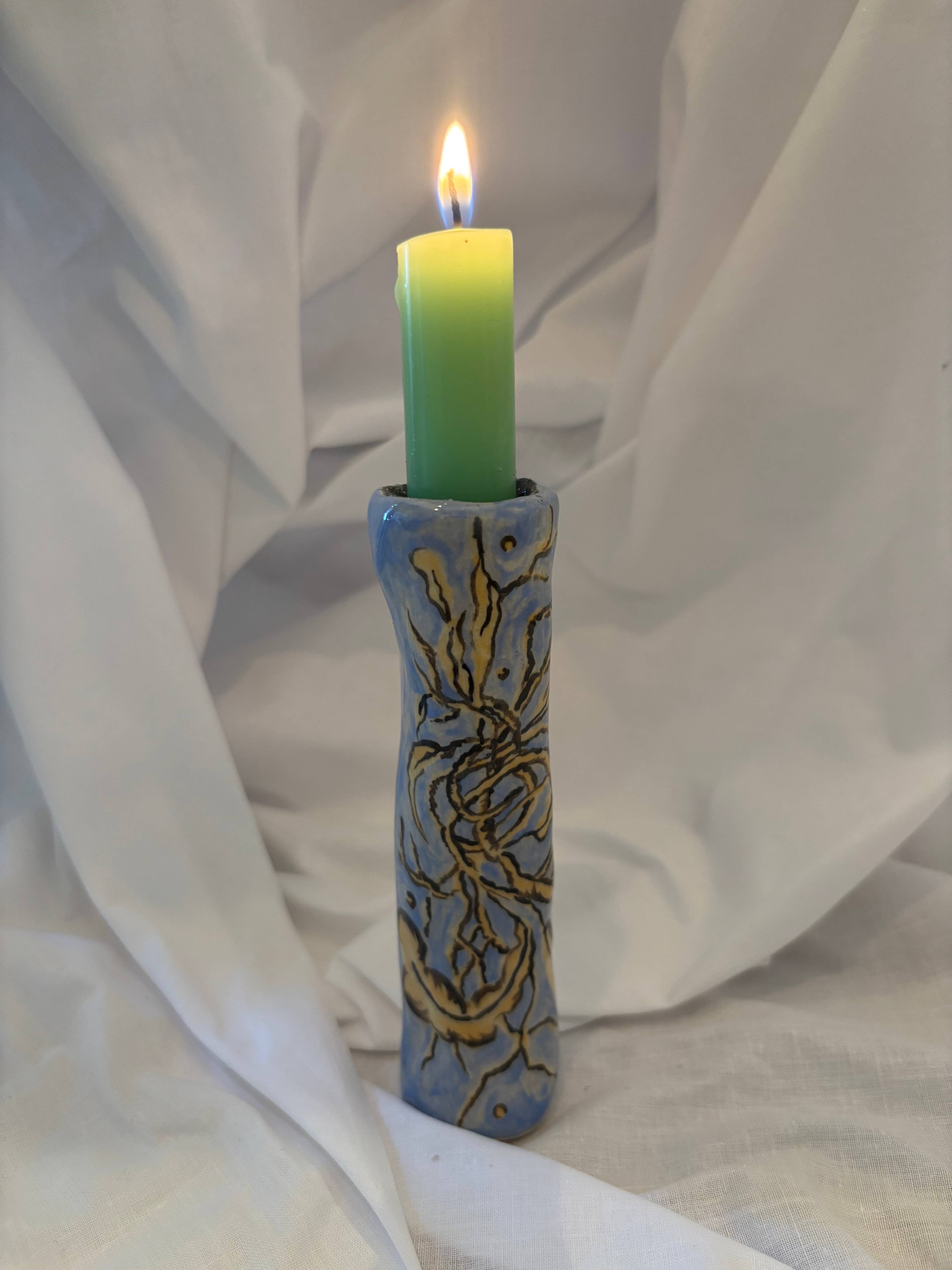 Candle in a decorative holder on a white fabric background.