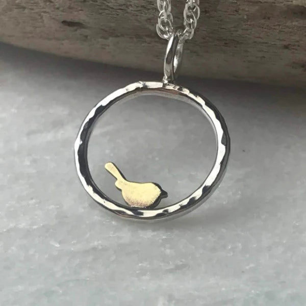 Silver pendant with a gold duck in the centre on a gray surface.