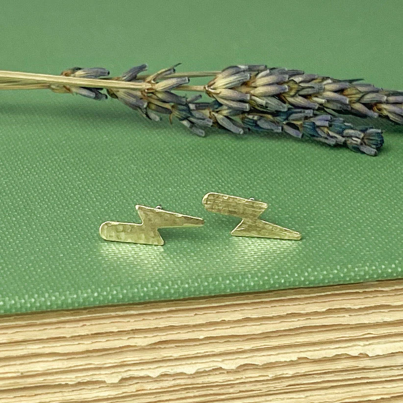 Gold lightning bolt earrings on a green textured surface with lavender.