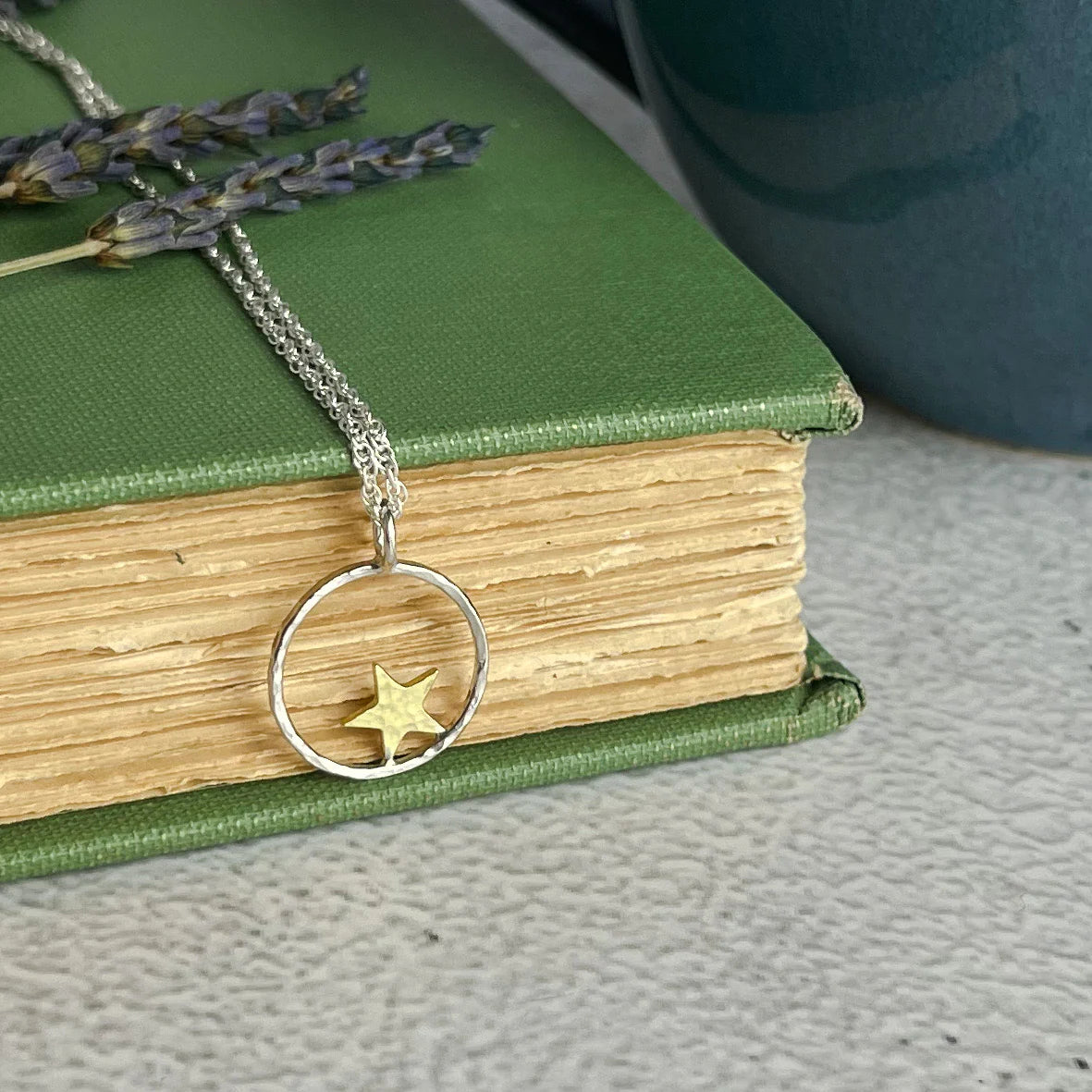 Silver necklace with a star pendant on a green book.