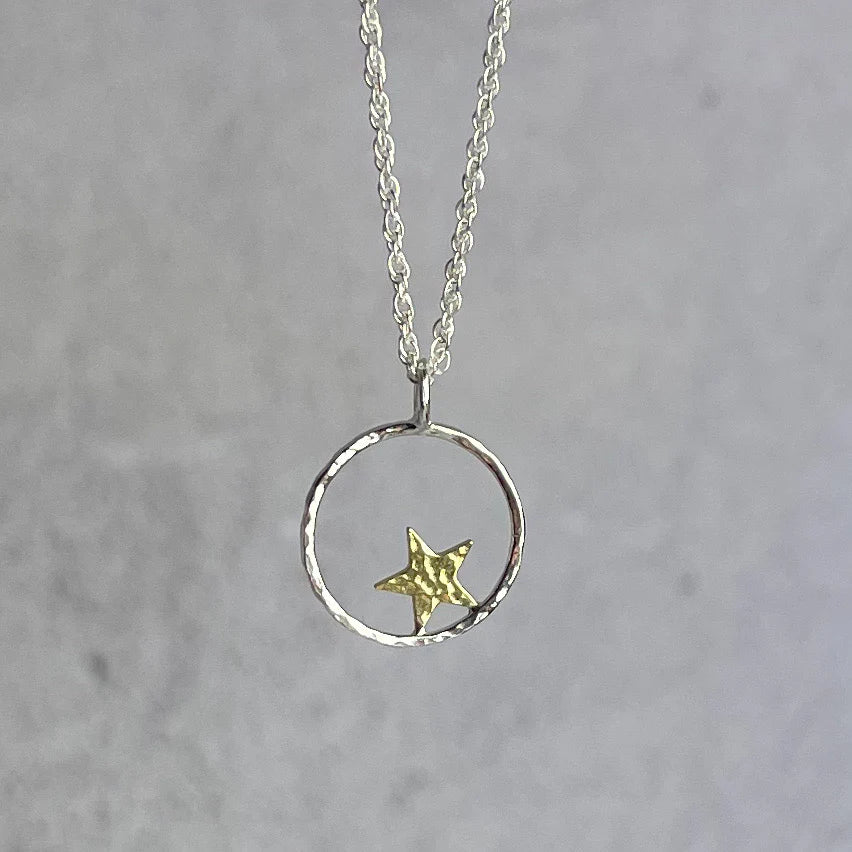 Necklace with a gold star pendant on a silver chain against a gray background.