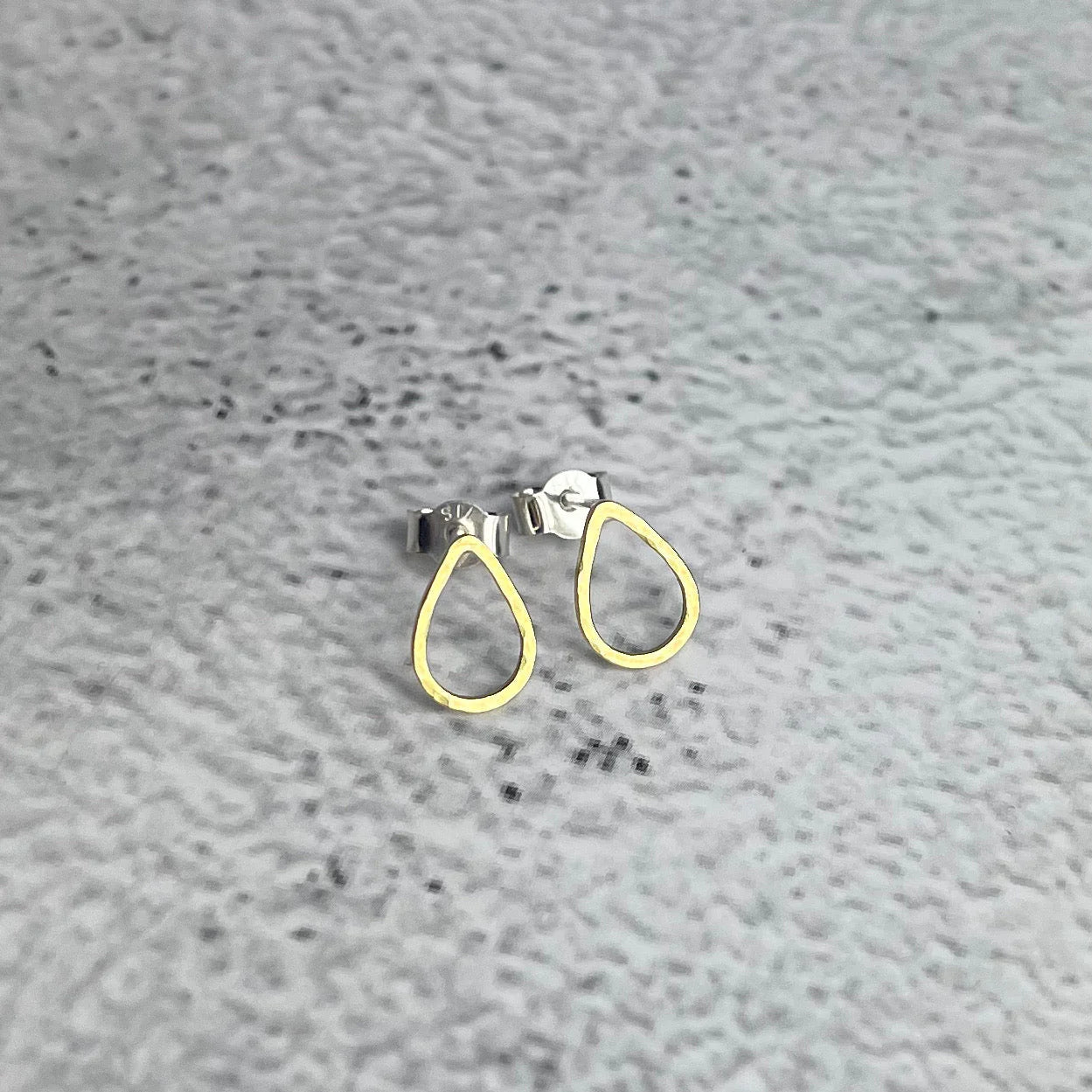 Gold teardrop earrings on a grey textured surface.