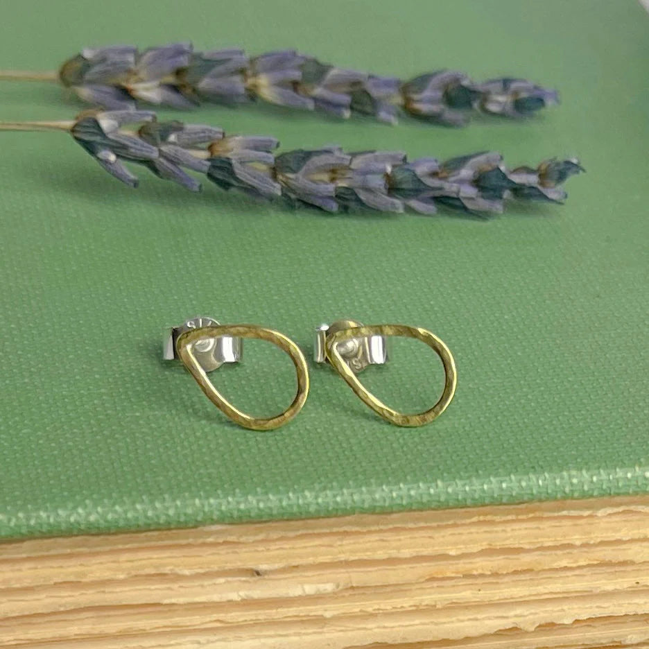 Gold hoop earrings on a green fabric surface with dried lavender flowers.