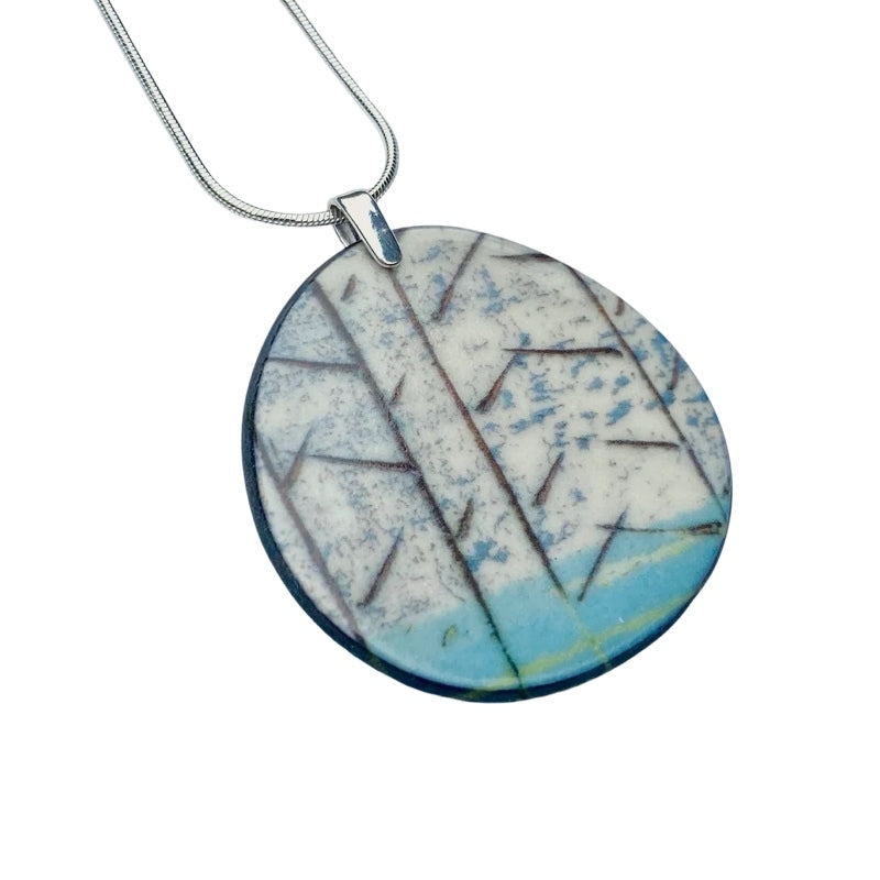 Oval porcelain pendant necklace with a turquoise base and black tree silhouettes on a 18 inch sterling silver chain.