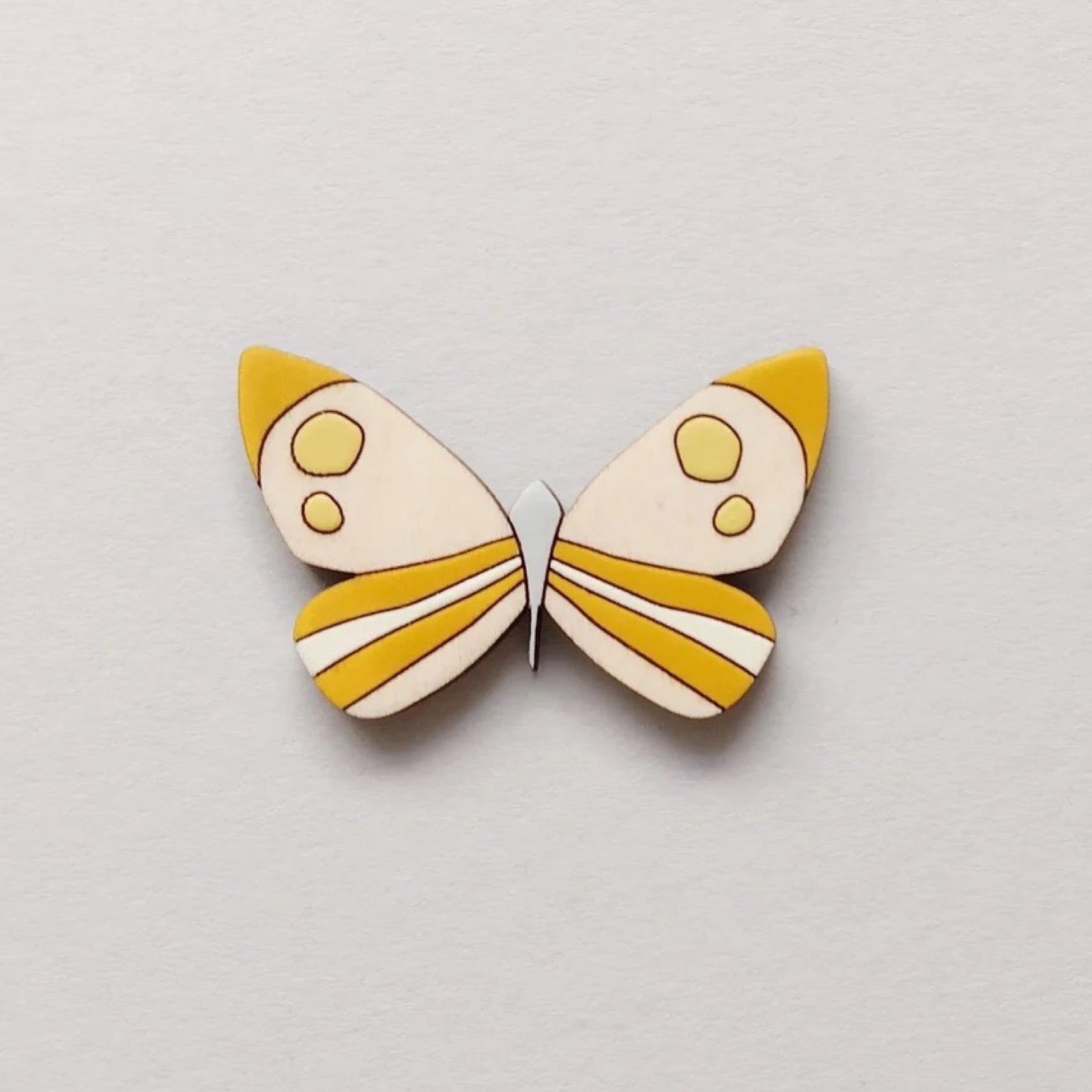 Butterfly brooch with yellow and white design on a light grey background.