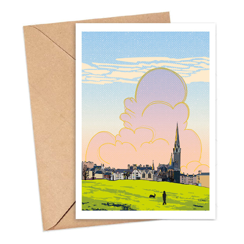 Greeting card with a scenic illustration of a town and large clouds, accompanied by a brown envelope.