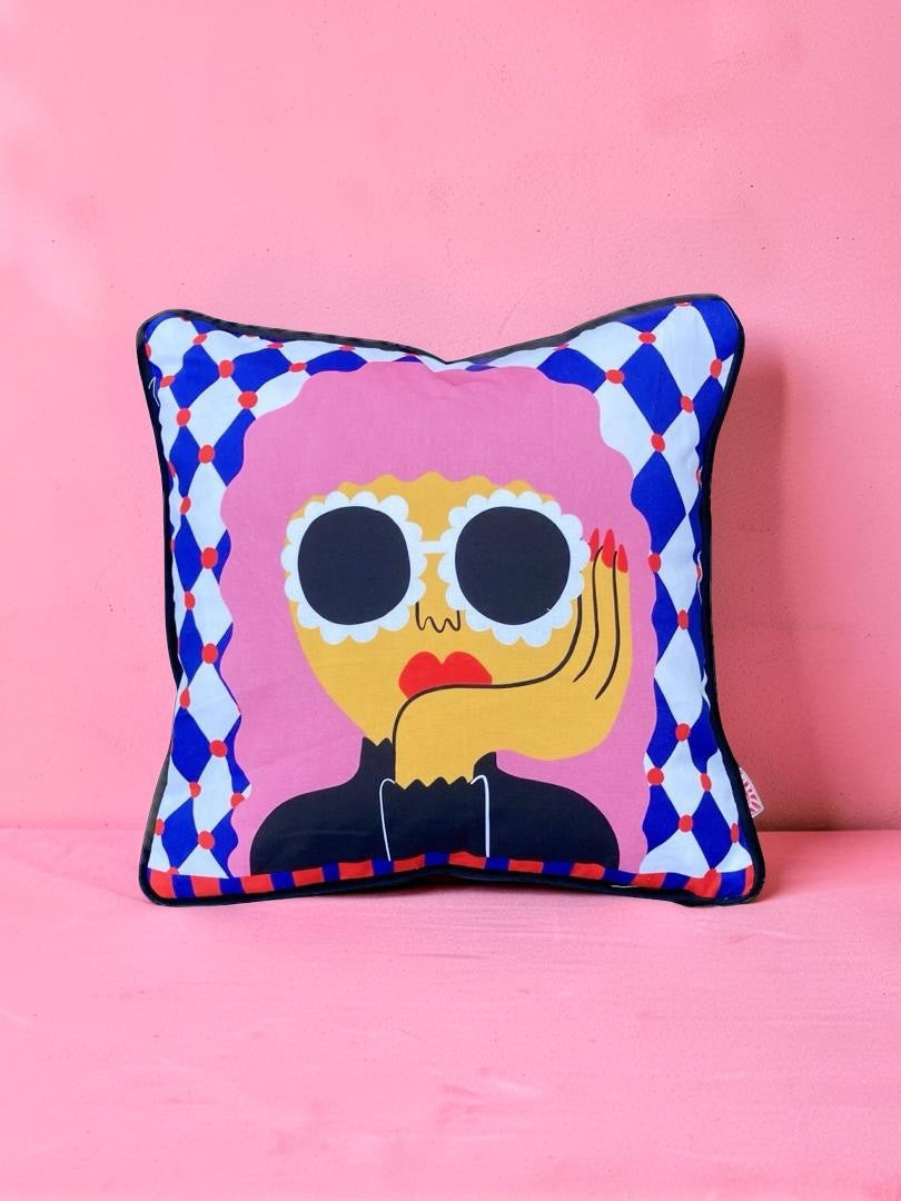 Decorative pillow with a colourful face design on a pink background.