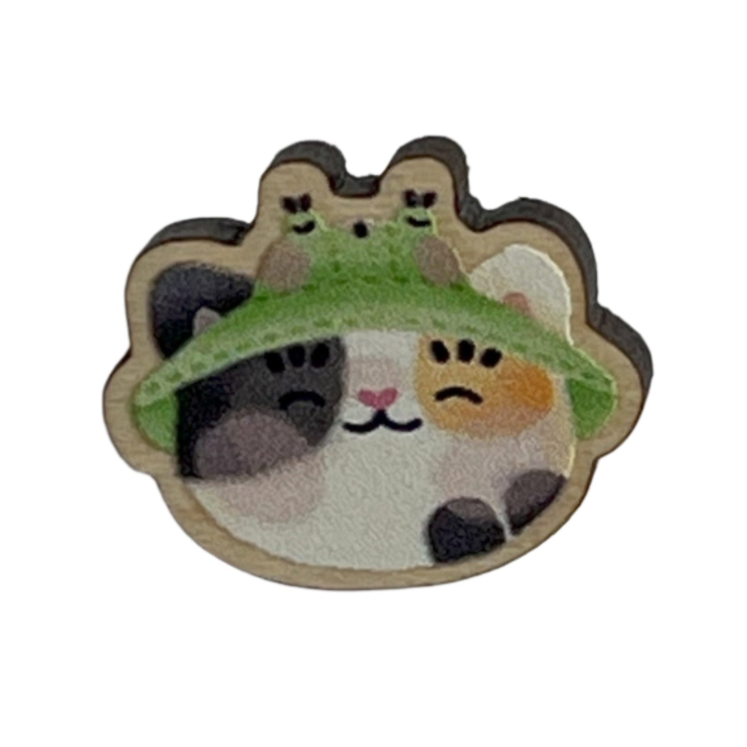 Mini wooden pin badge of a calico cat wearing a frog bucket hat. 