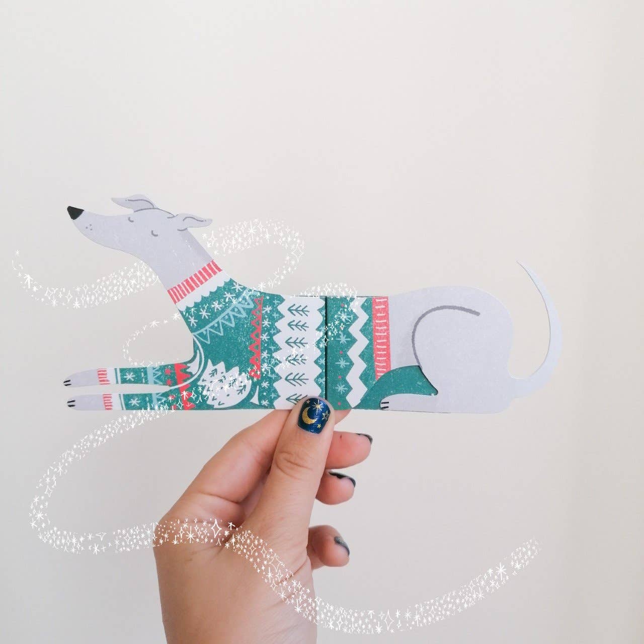 Hand holding a paper dog card with a sweater against a light background.
