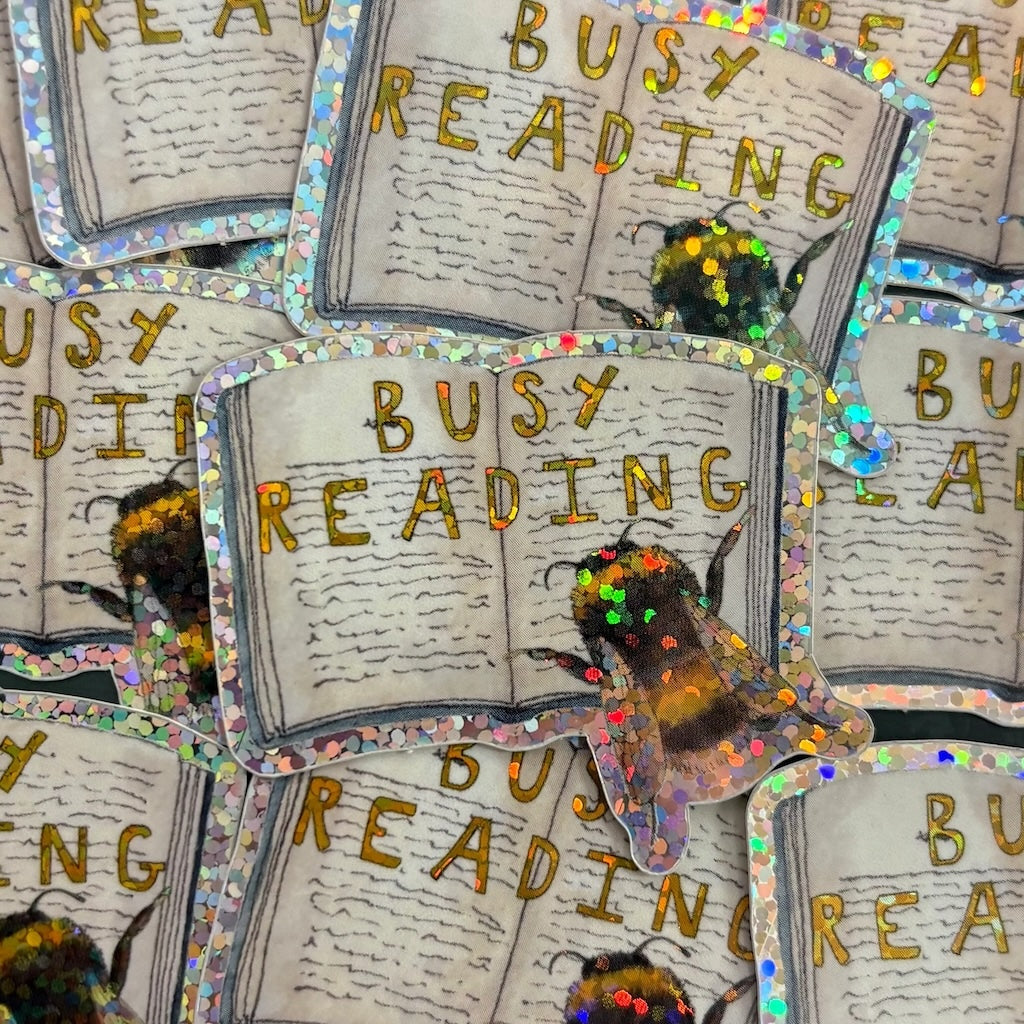 Vinyl sticker of open pages of a book with a bee in the corner and the text 'Busy Reading'.