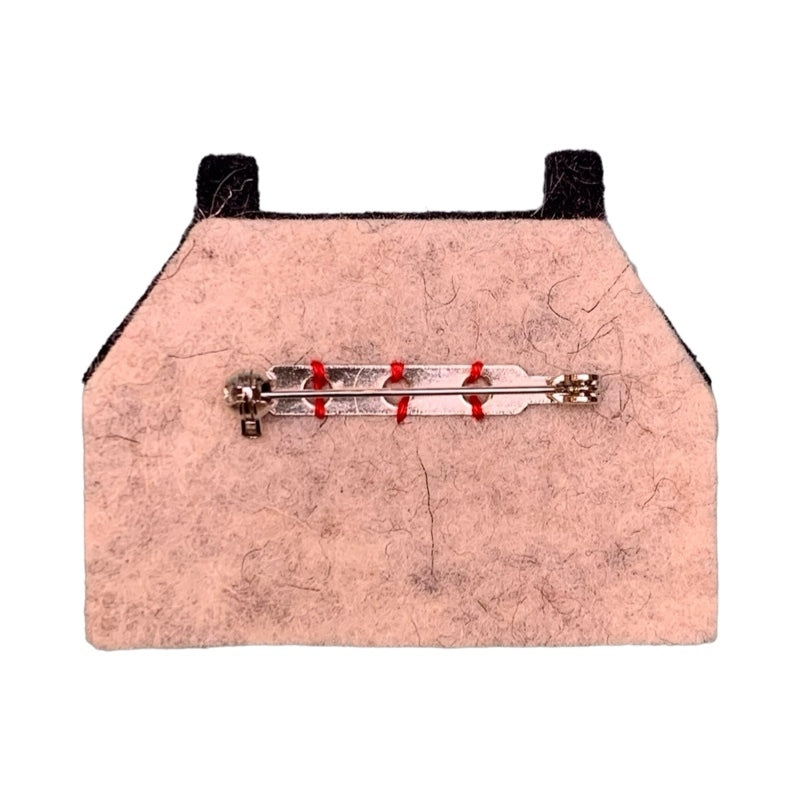Felt brooch of a traditional Scottish but 'n' ben featuring a white structure with a black roof and windows and a red door.