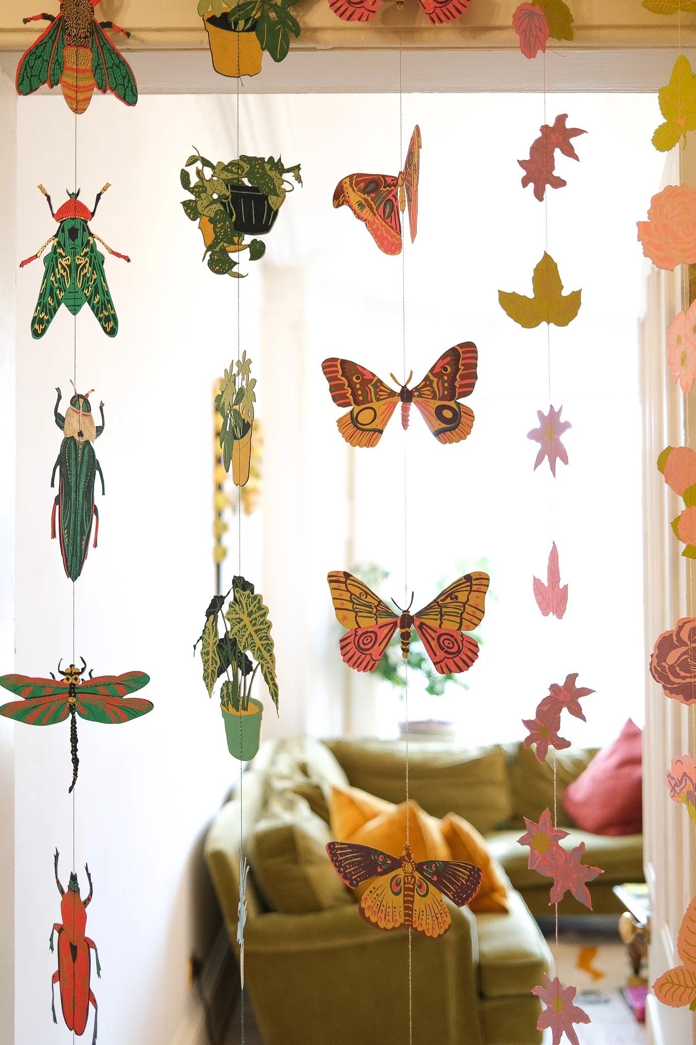 Decorative string with colourful paper insects, butterflies, plants and flowers hanging in a room.