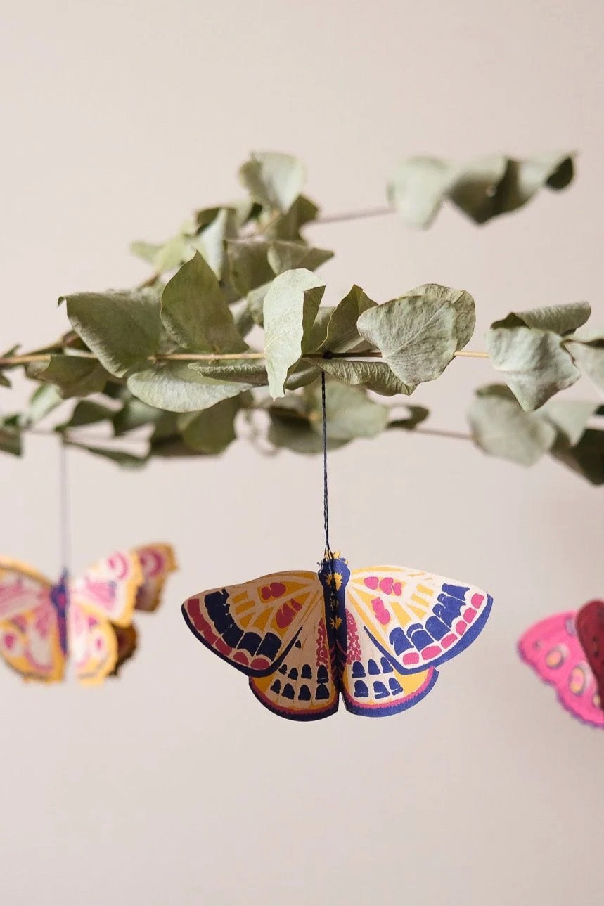 Colourful butterfly decorations hanging from a branch with green leaves.
