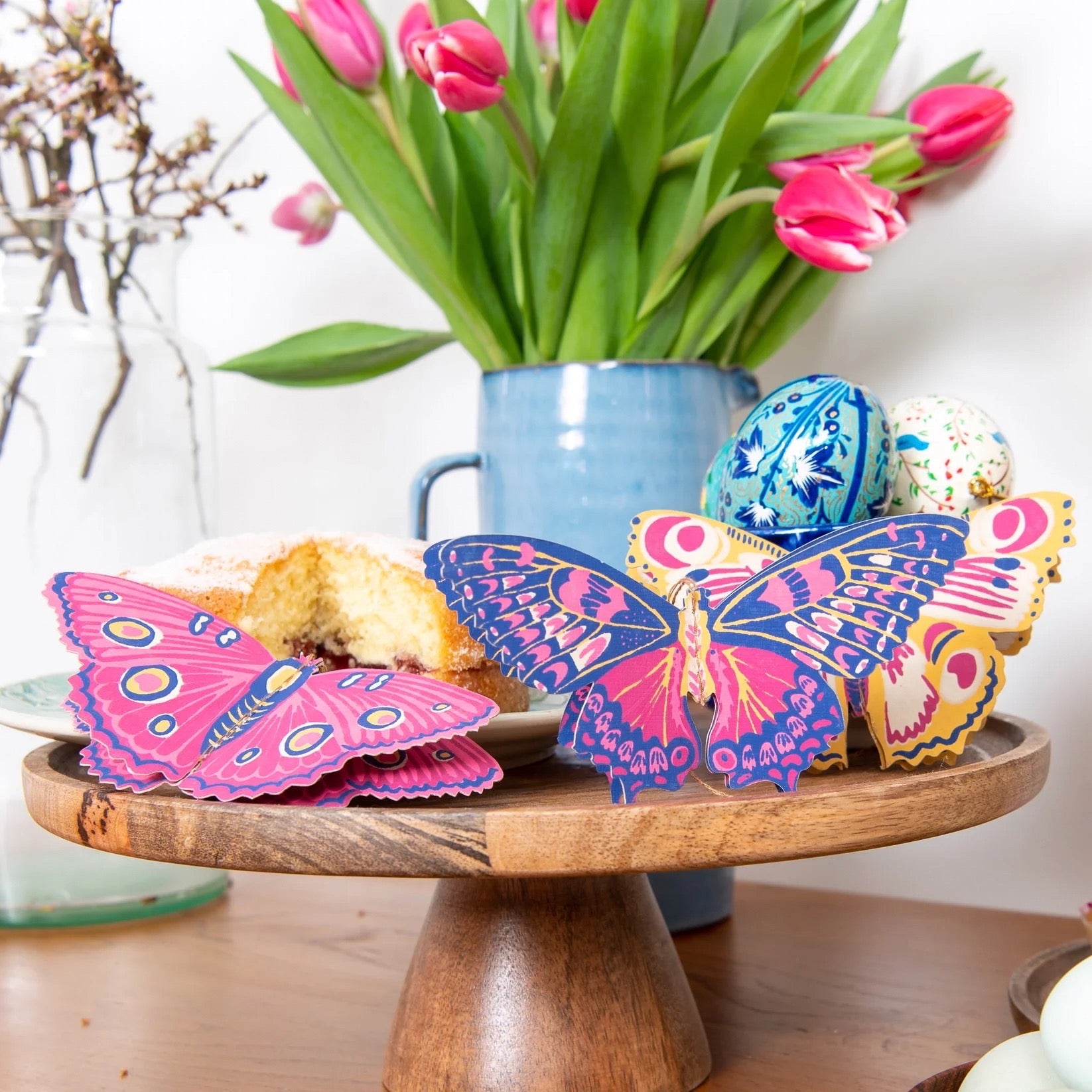 Colourful butterfly decorations on a table next to flowers and a cake.