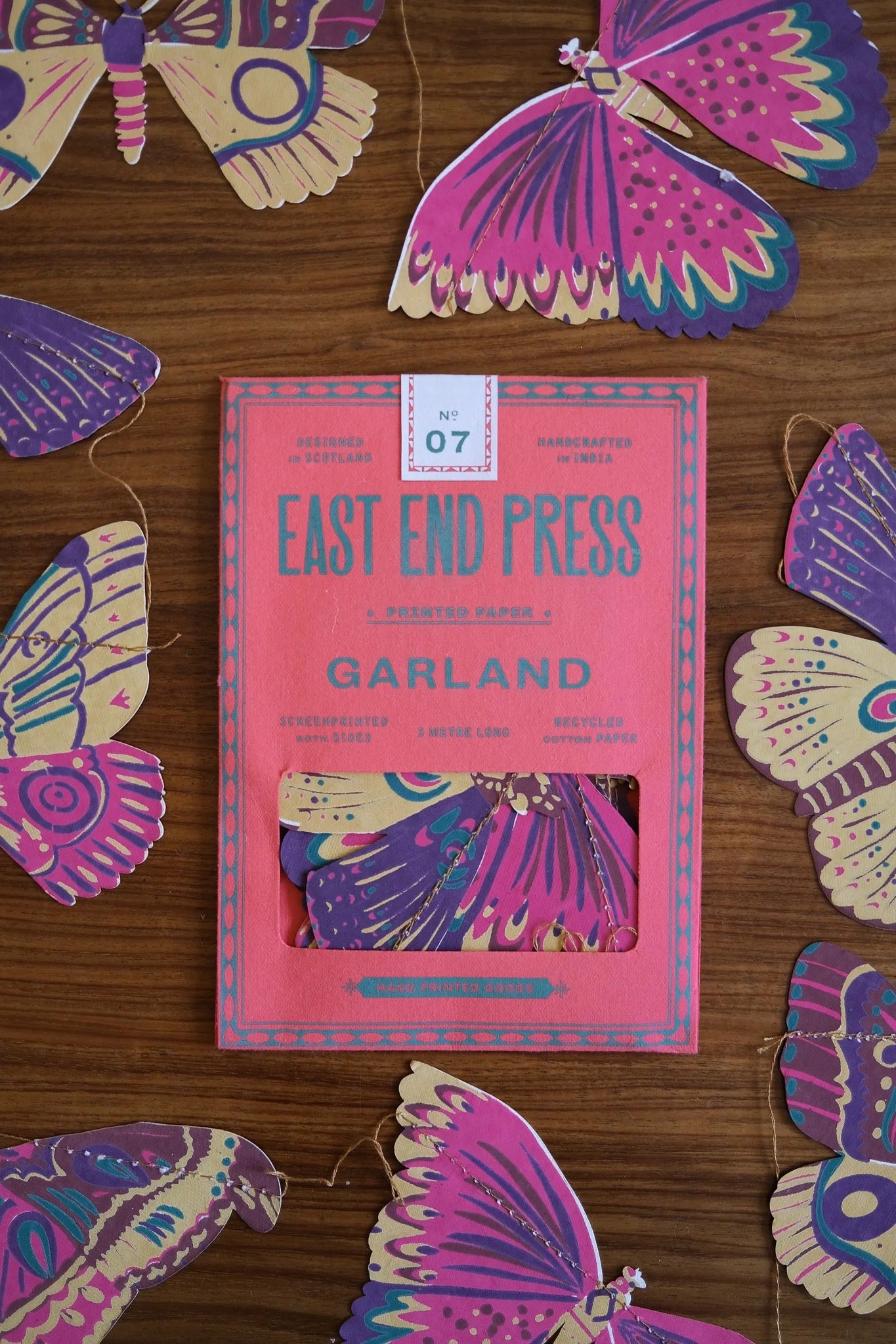 Pink packaging by East End Press surrounded by colourful butterfly-shaped paper cutouts on a wooden surface.