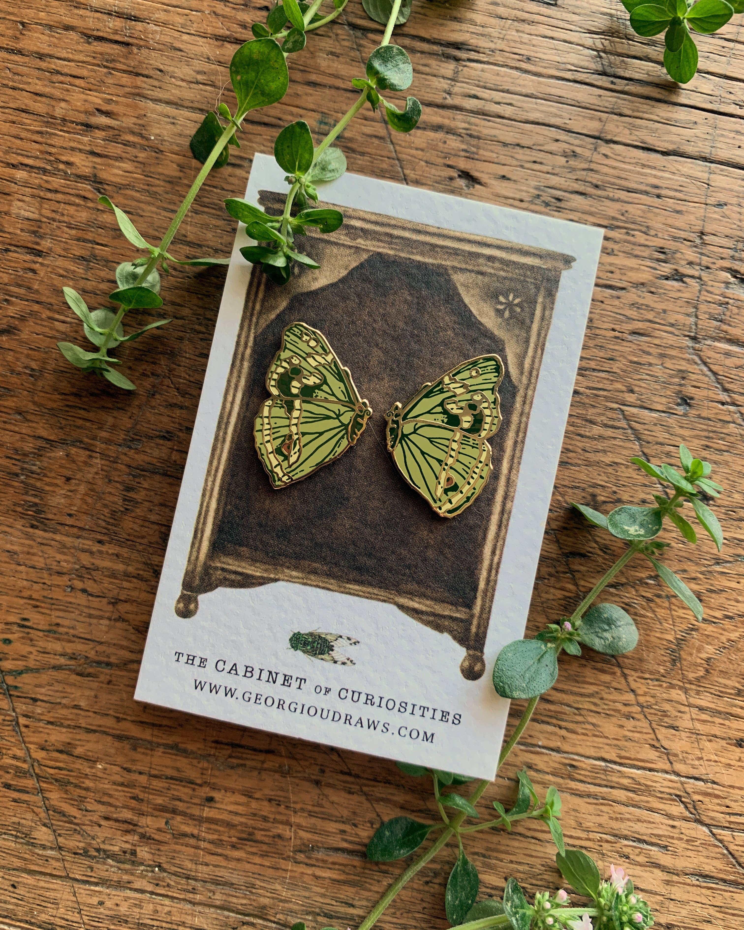 Butterfly-shaped pin badges on a card with green leaves around on a wooden surface.