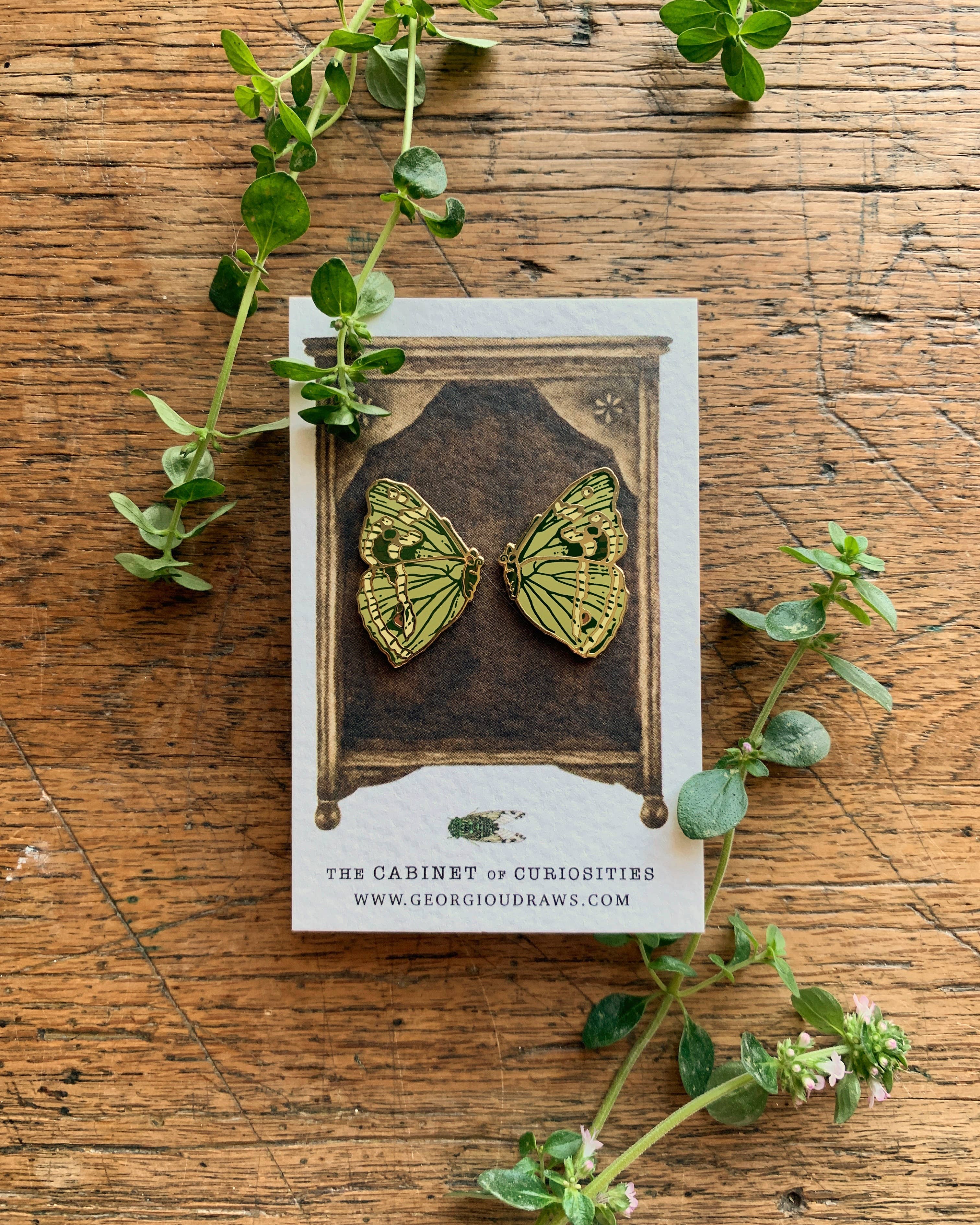 Butterfly-shaped pin badges on a card with green leaves on a wooden surface.