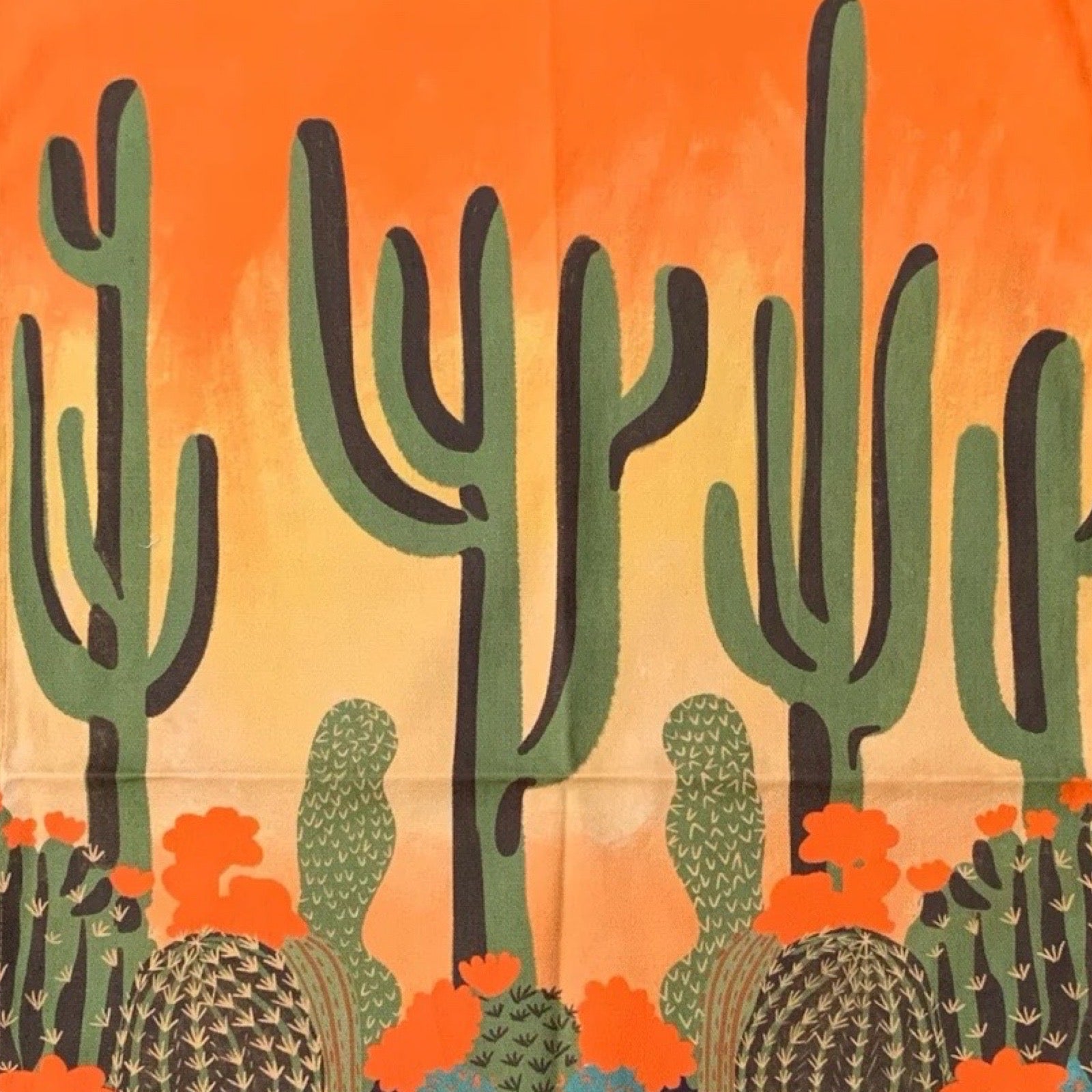 Close up of a tea towel with a cactus design on an orange background.