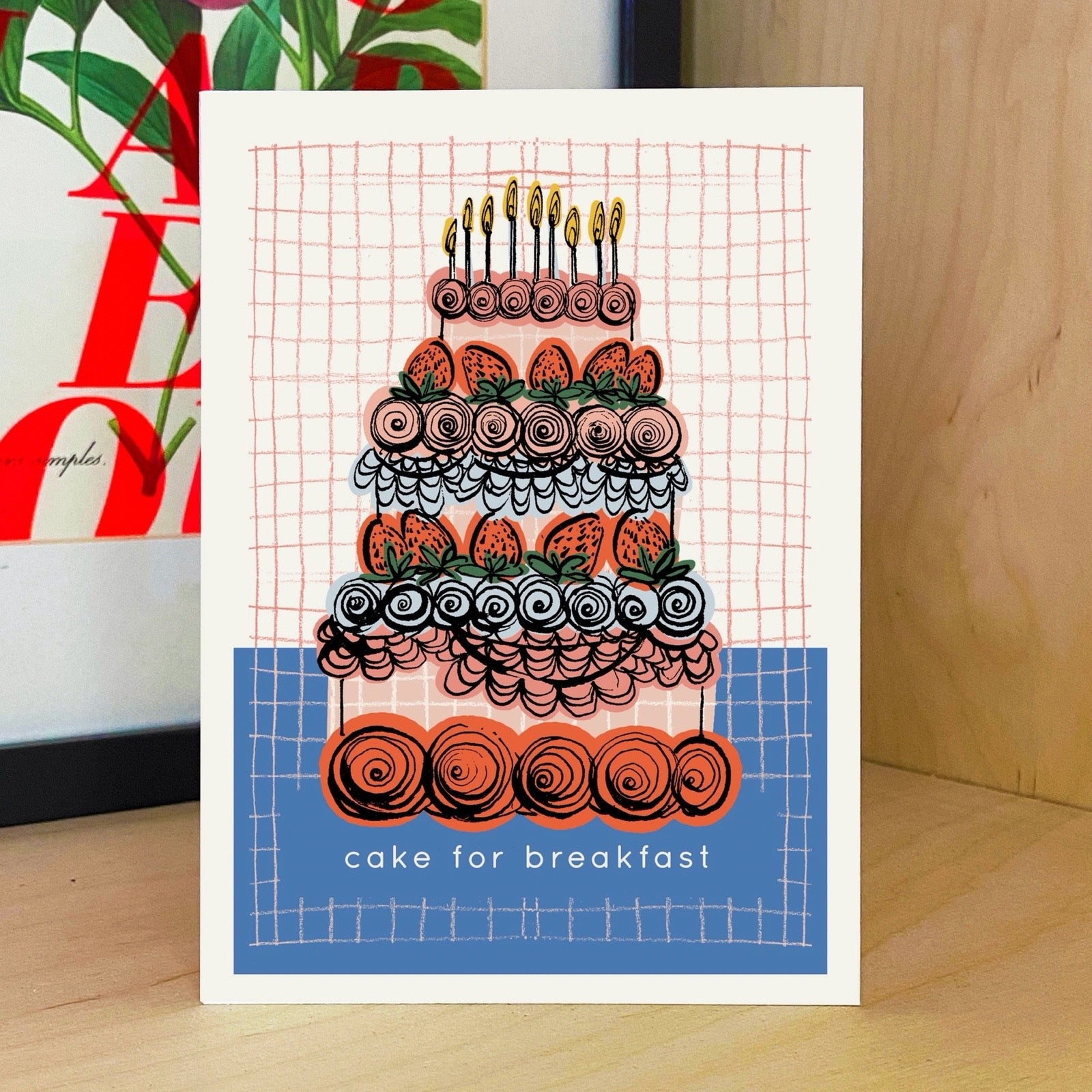 Card with a colourful cake illustration and 'cake for breakfast' text on a grid background.
