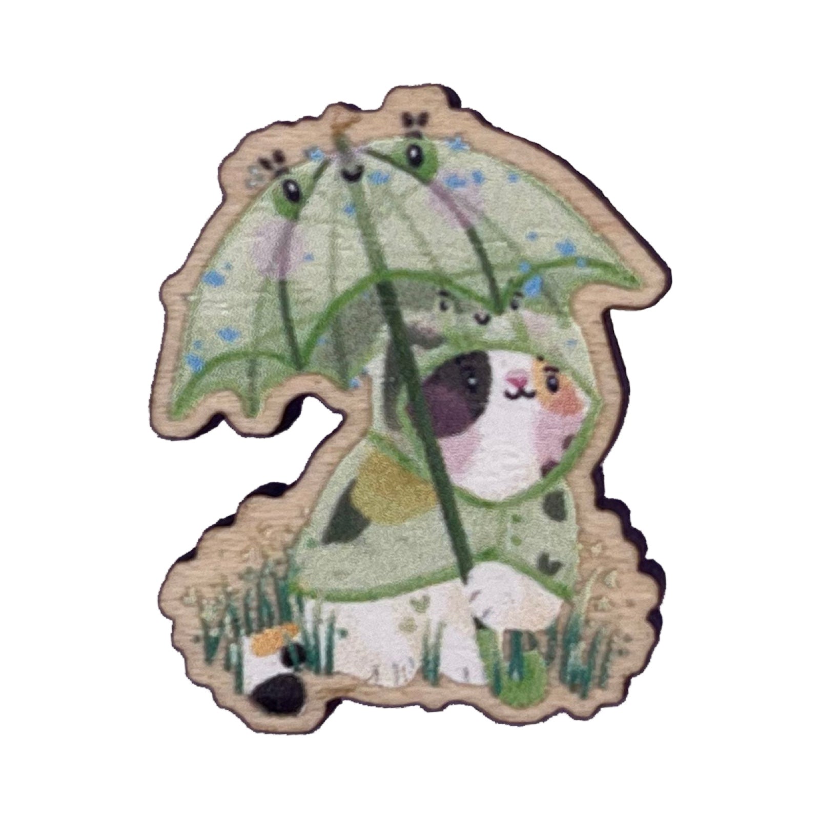 Wooden pin badge of a calico cat wearing a frog raincoat, holding a matching frog umbrella.