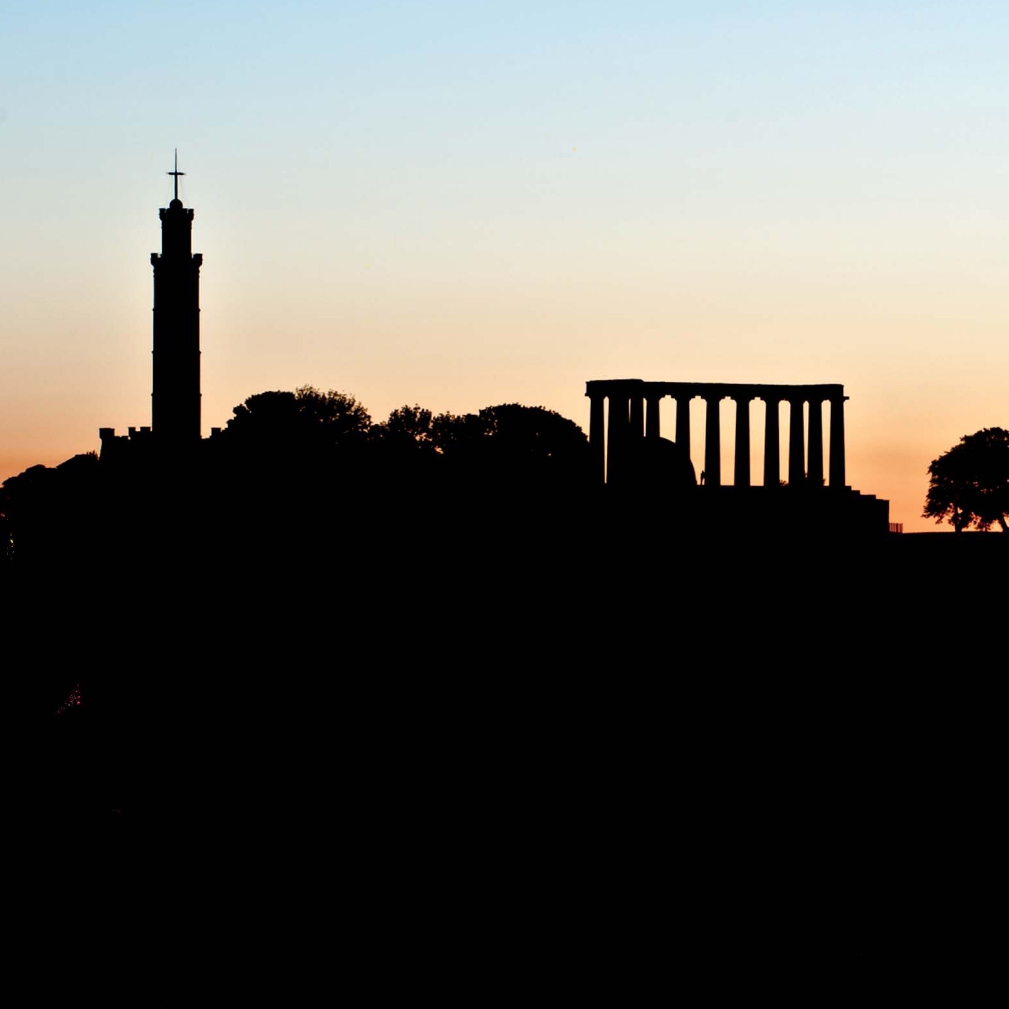 Silhouette of Calton Hill Edinburgh against a sunset sky.