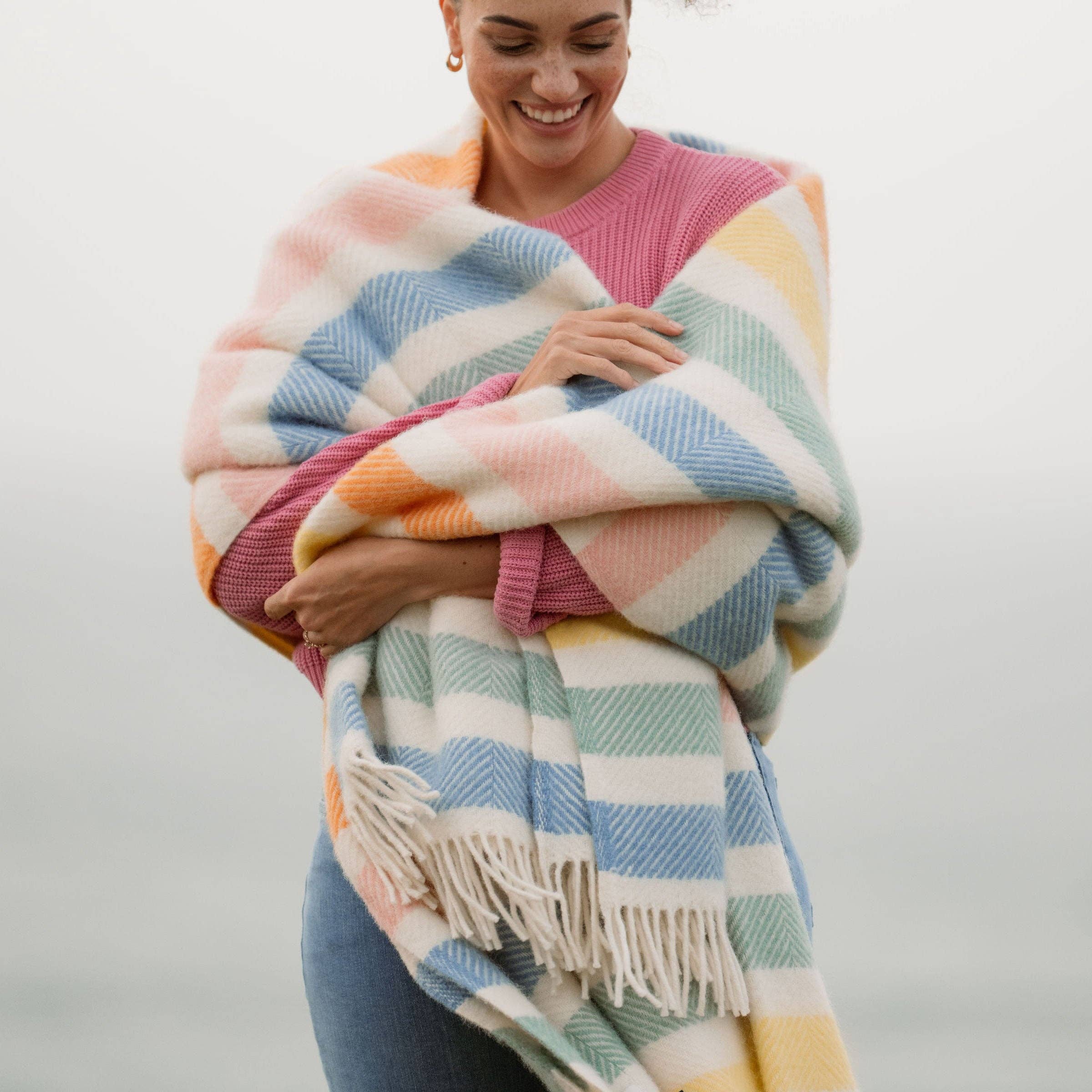 Striped wool blanket with yellow, green, blue, pink and cream stripes with cream fringing on a woman.