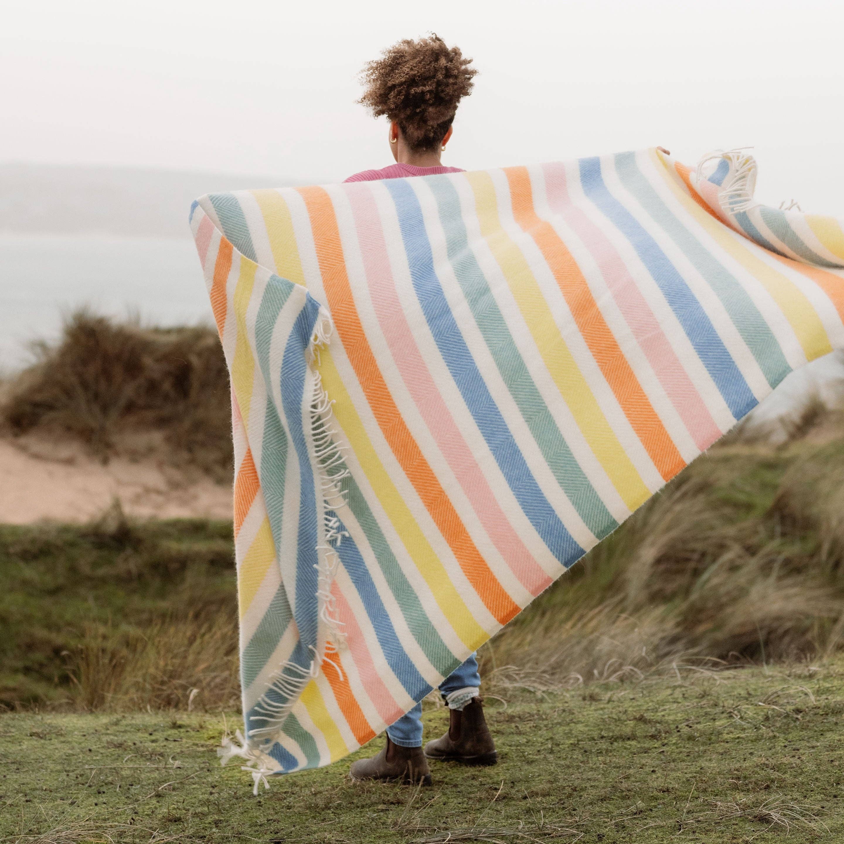 Striped wool blanket with yellow, green, blue, pink and cream stripes with cream fringing on a woman.