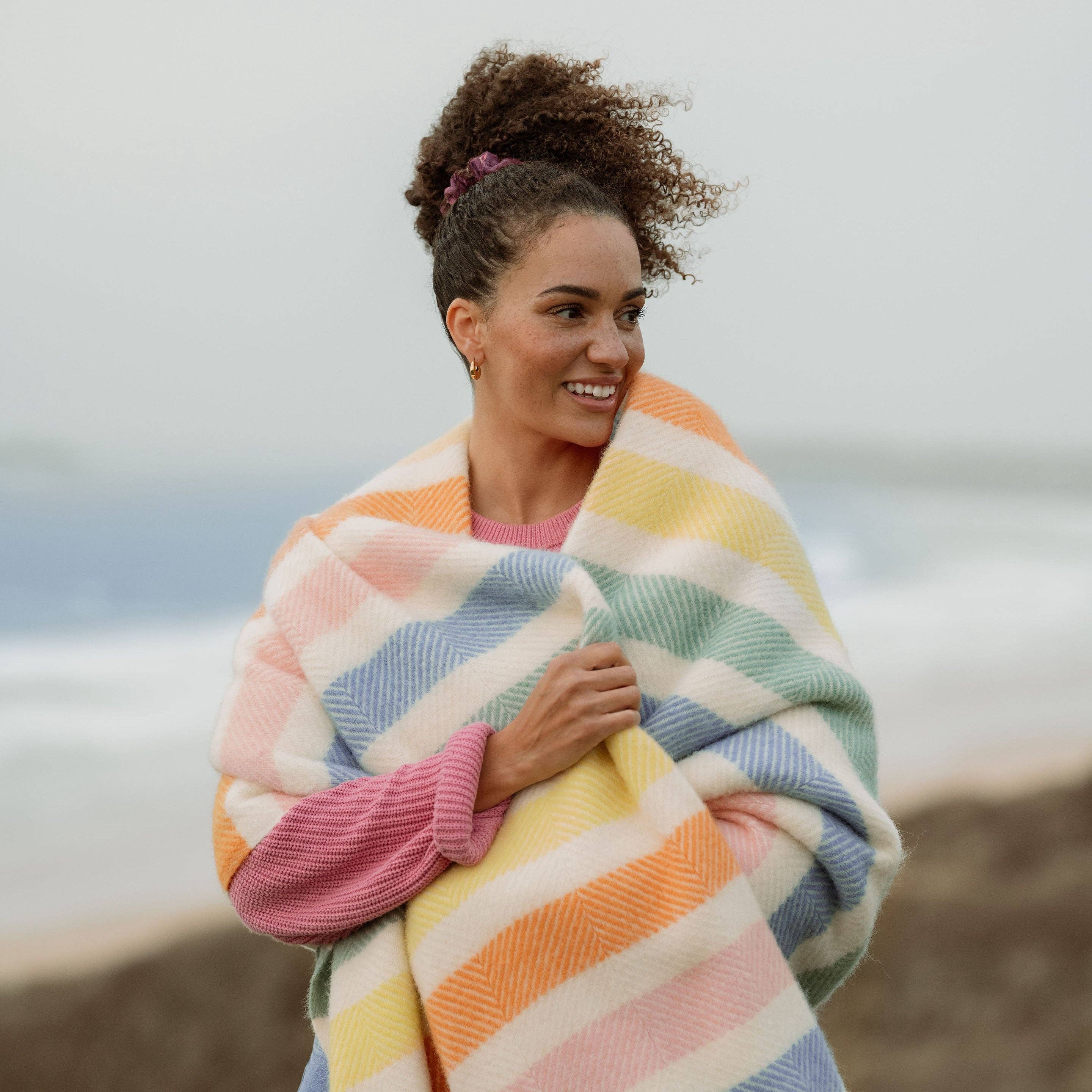 Striped wool blanket with yellow, green, blue, pink and cream stripes with cream fringing on a woman.
