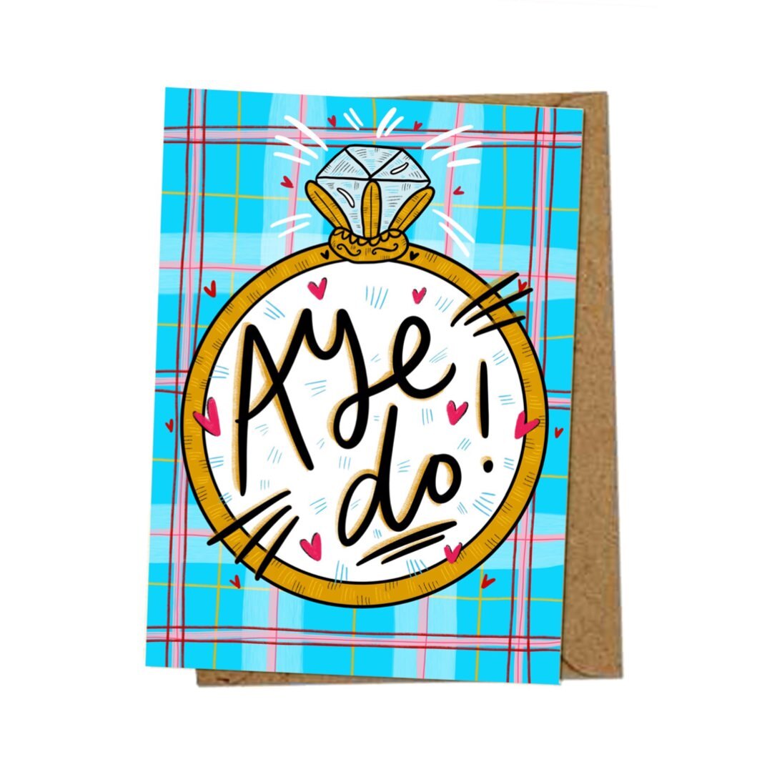 Engagement card featuring a huge diamond ring with the text 'Aye Do' inside and on a blue and pink tartan background.