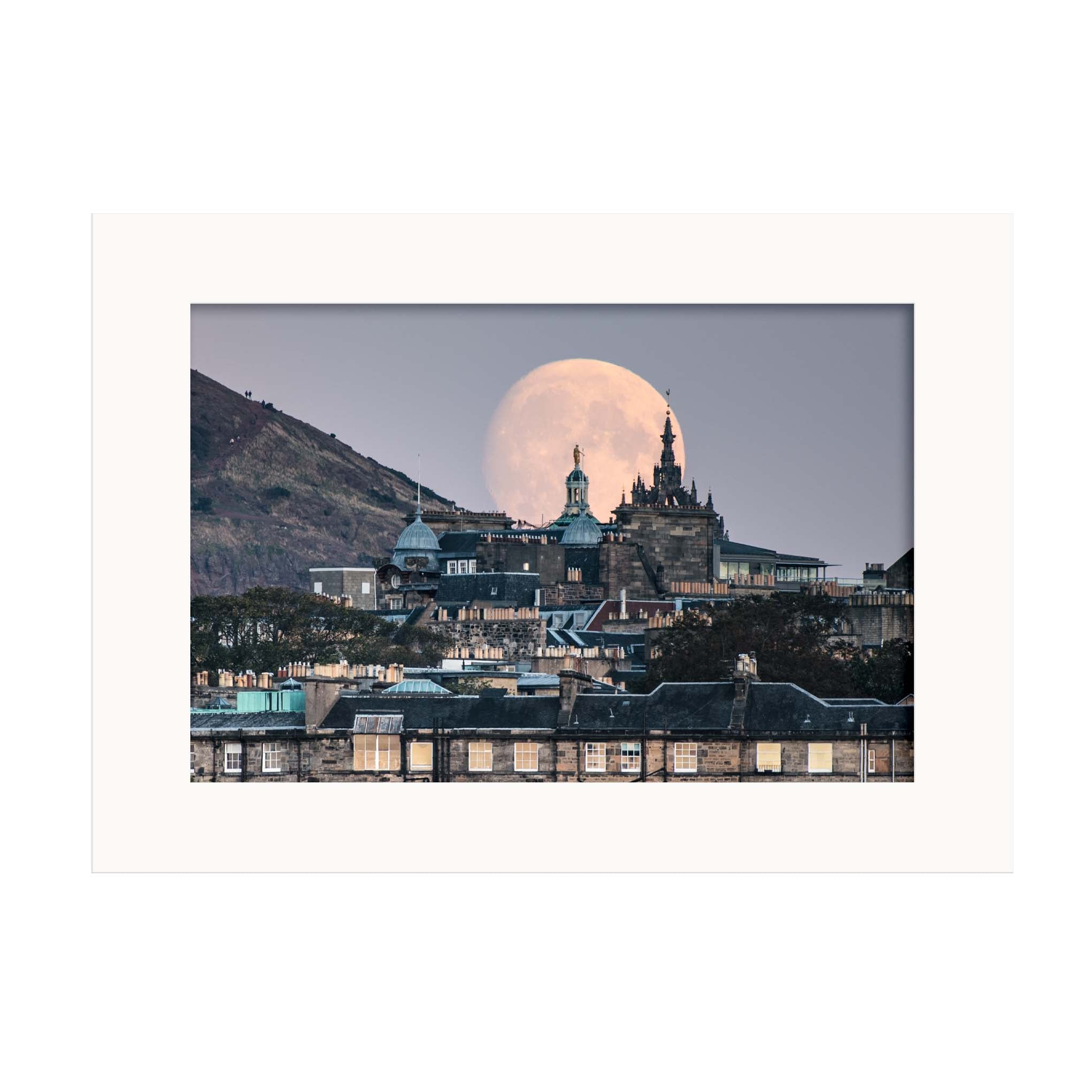 An image of a moon rising behind some buildings in a white mount. 