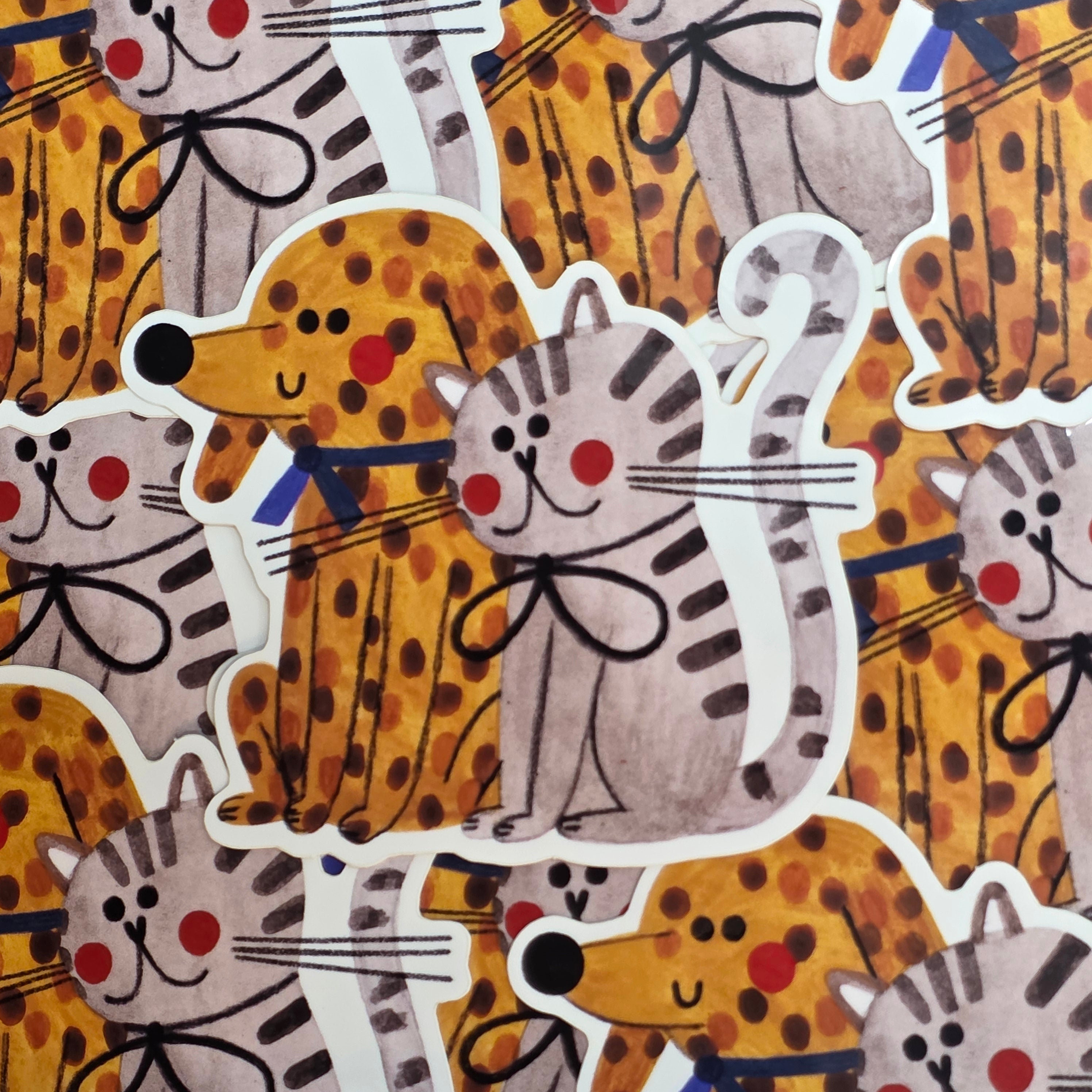 This vinyl sticker features a ginger spotty dog and a grey and black cat both with rosy cheeks.
