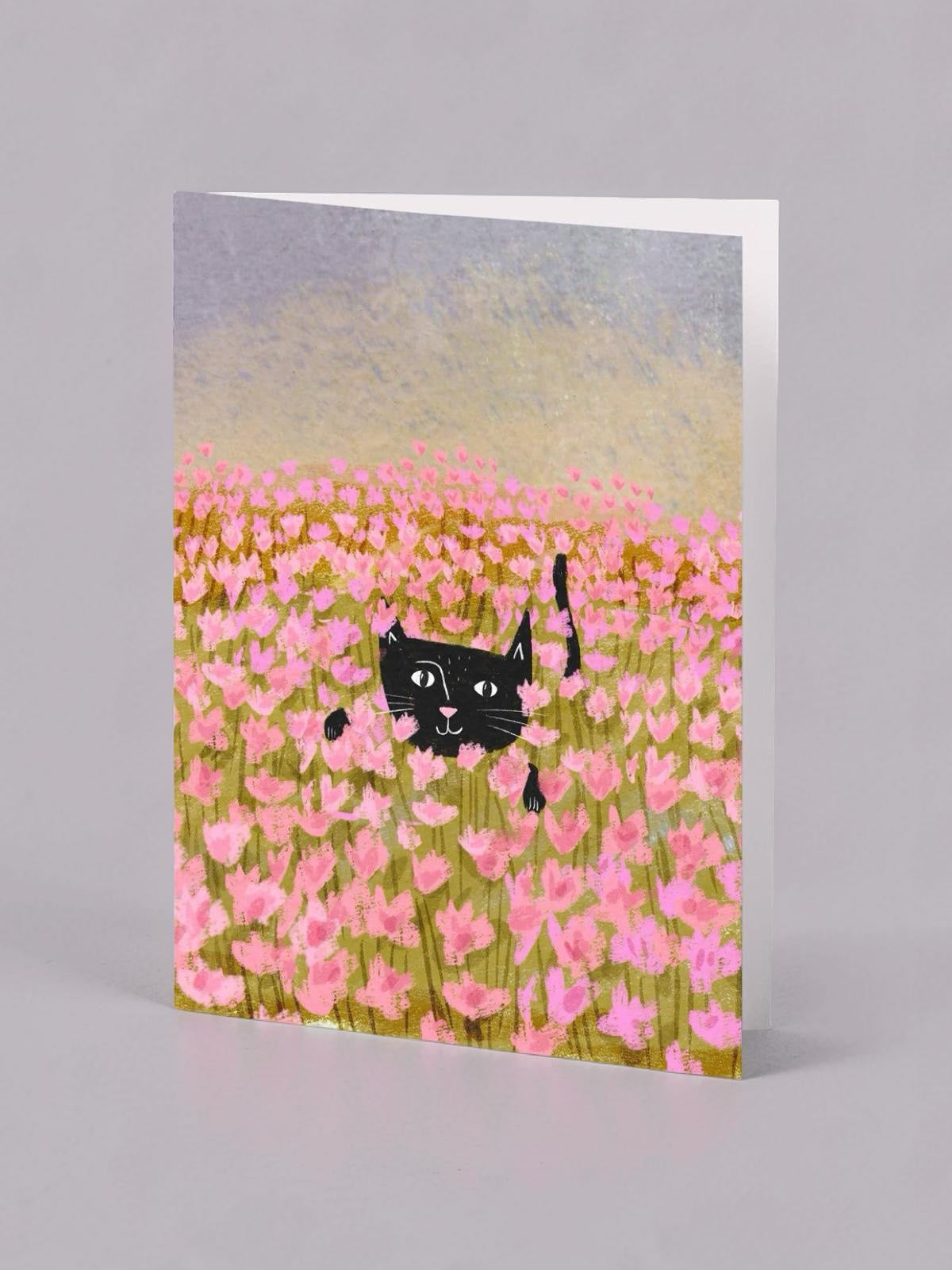Card with a black cat in a field of pink flowers on a gray background.