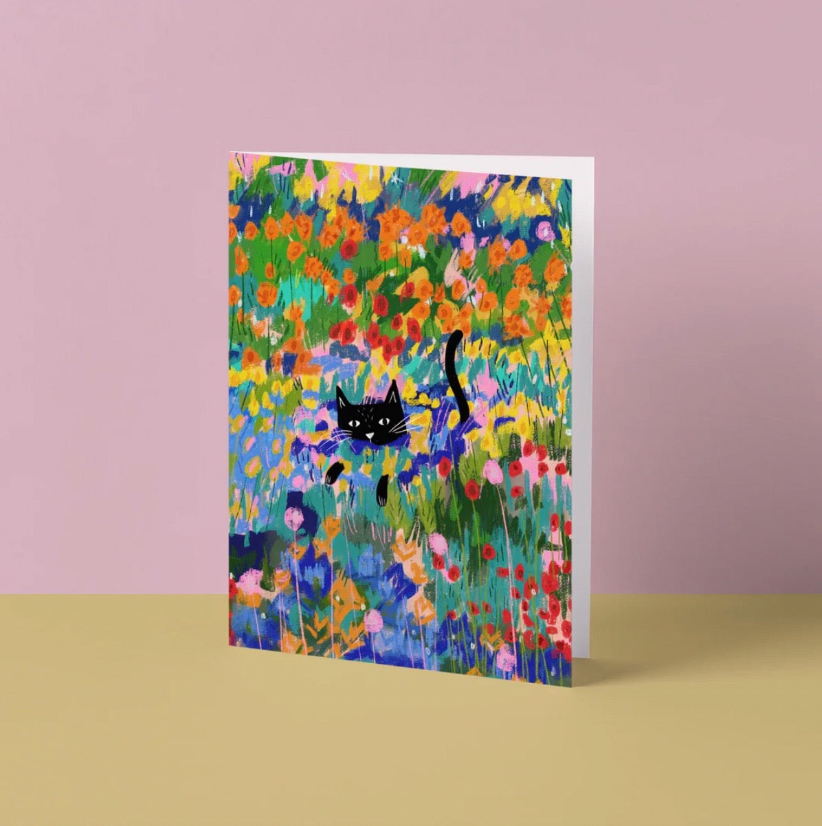 Greeting card with a black cat among colourful flowers on a pink background.