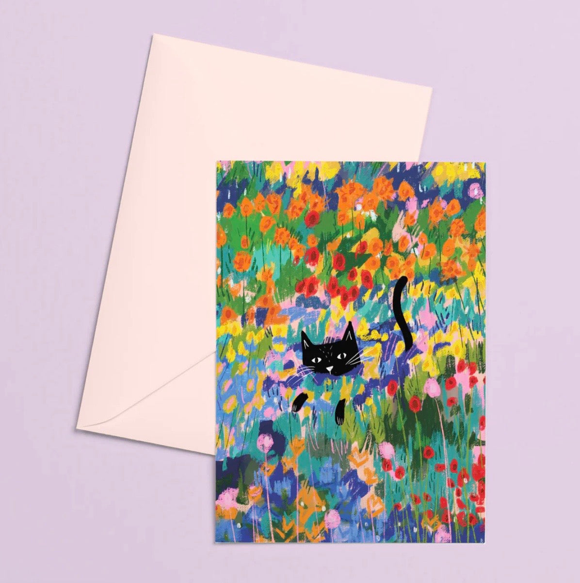 Greeting card with a black cat in a colourful floral field and matching envelope on a light purple background.